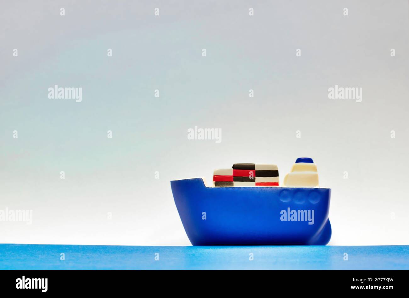 Blaues Spielzeug-Frachtschiff, das auf ruhigen Meeren mit einem trüben Himmel im Hintergrund mit Kopierraum und geringer Schärfentiefe segelt. Konzept der Seefracht-Logistik. Stockfoto