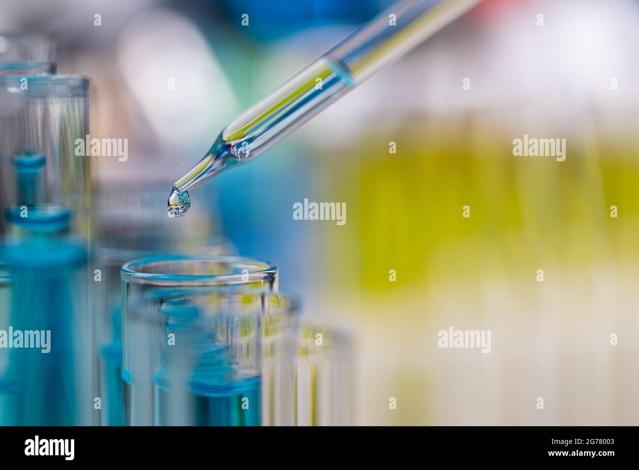Tropfen blauer Flüssigkeit vom Tropfen zum Reagenzglas im Labor mit heller Farbunschärfe im Hintergrund. Stockfoto
