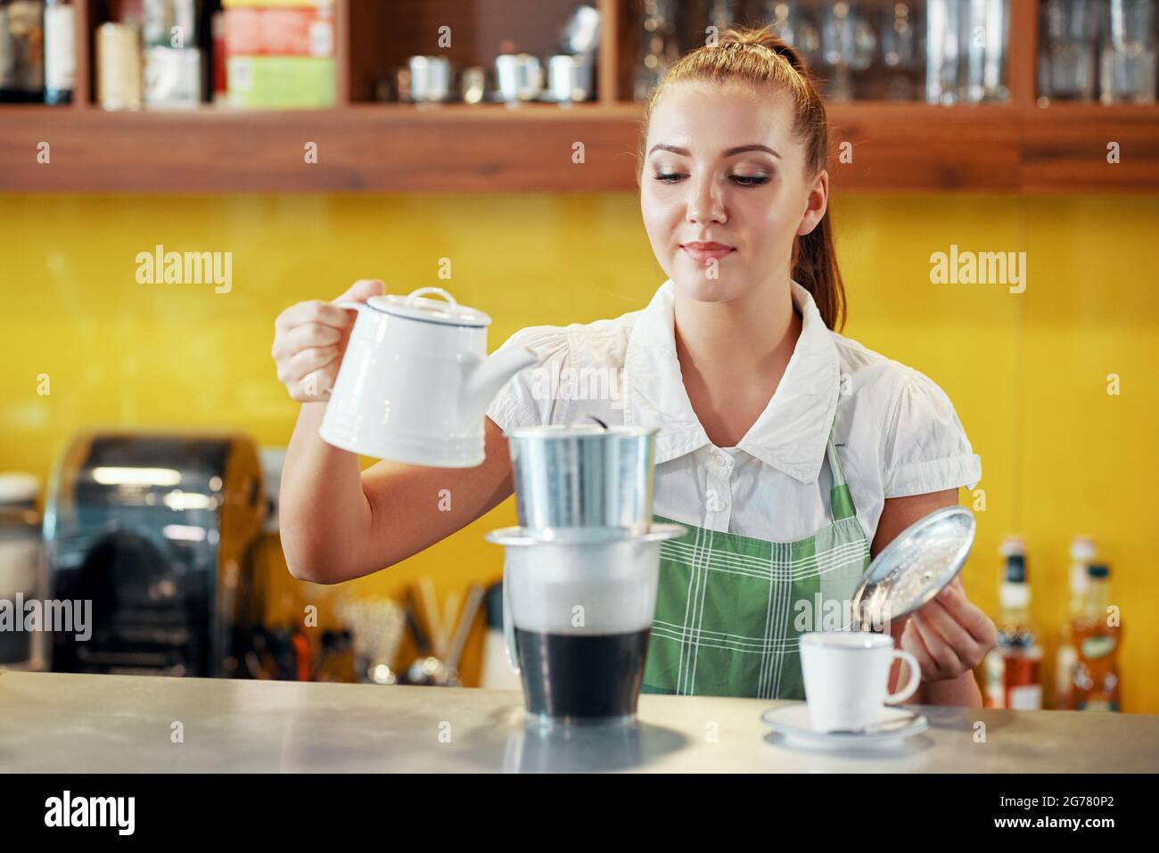 Junge Kellnerin, die vietnamesischen heißen Milchkaffee für Kunden macht, gießt sie Wasser in den phinfilter Stockfoto