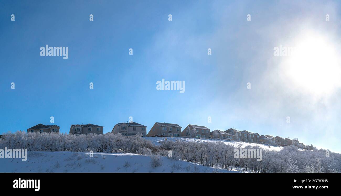 Klar, hell und sonnig an einem Wintertag, der auf einem schneebedeckten Feld mit einer Reihe von Häusern im Hintergrund leuchtet Stockfoto