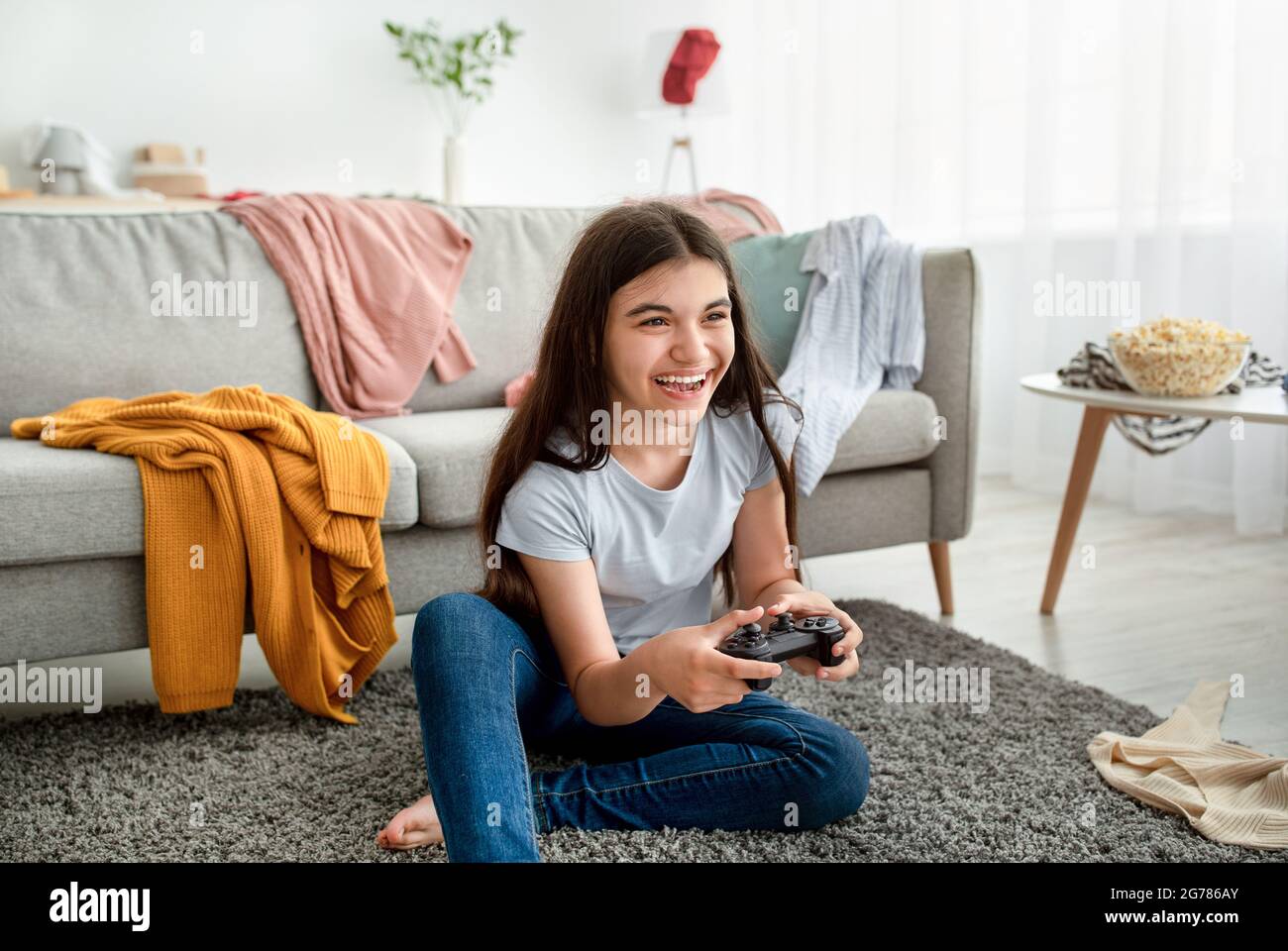 Happy Indian Teenager mit Joystick spielen Online-Computerspiele in chaotischen Raum während covid Lockdown Stockfoto