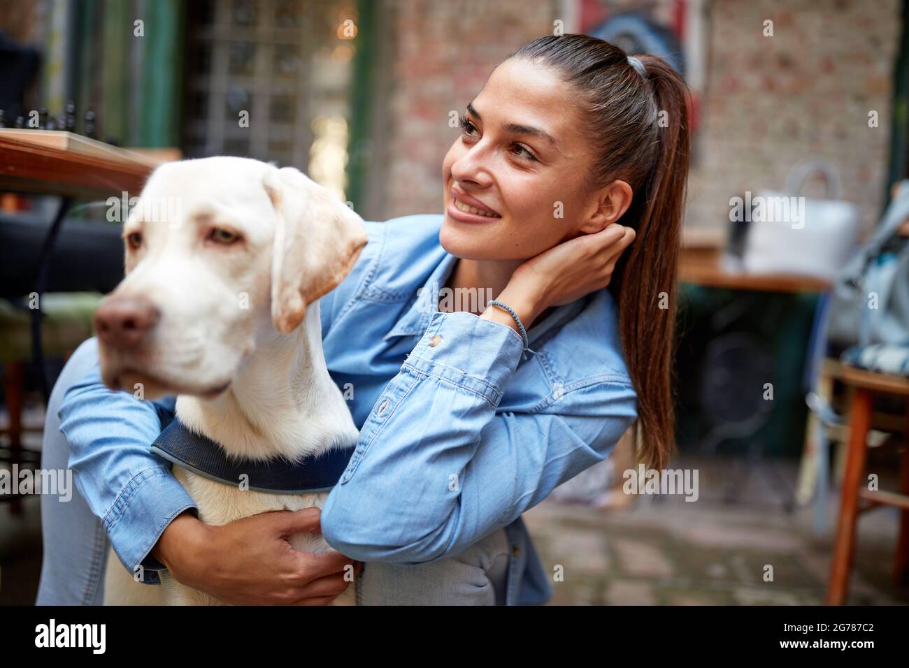 Ein junges schönes Mädchen in einer Umarmung mit ihrem Hund, während sie eine Zeit in einer angenehmen Atmosphäre in der Bar zusammen verbringen. Freizeit, Bar, Freundschaft, Outdoo Stockfoto