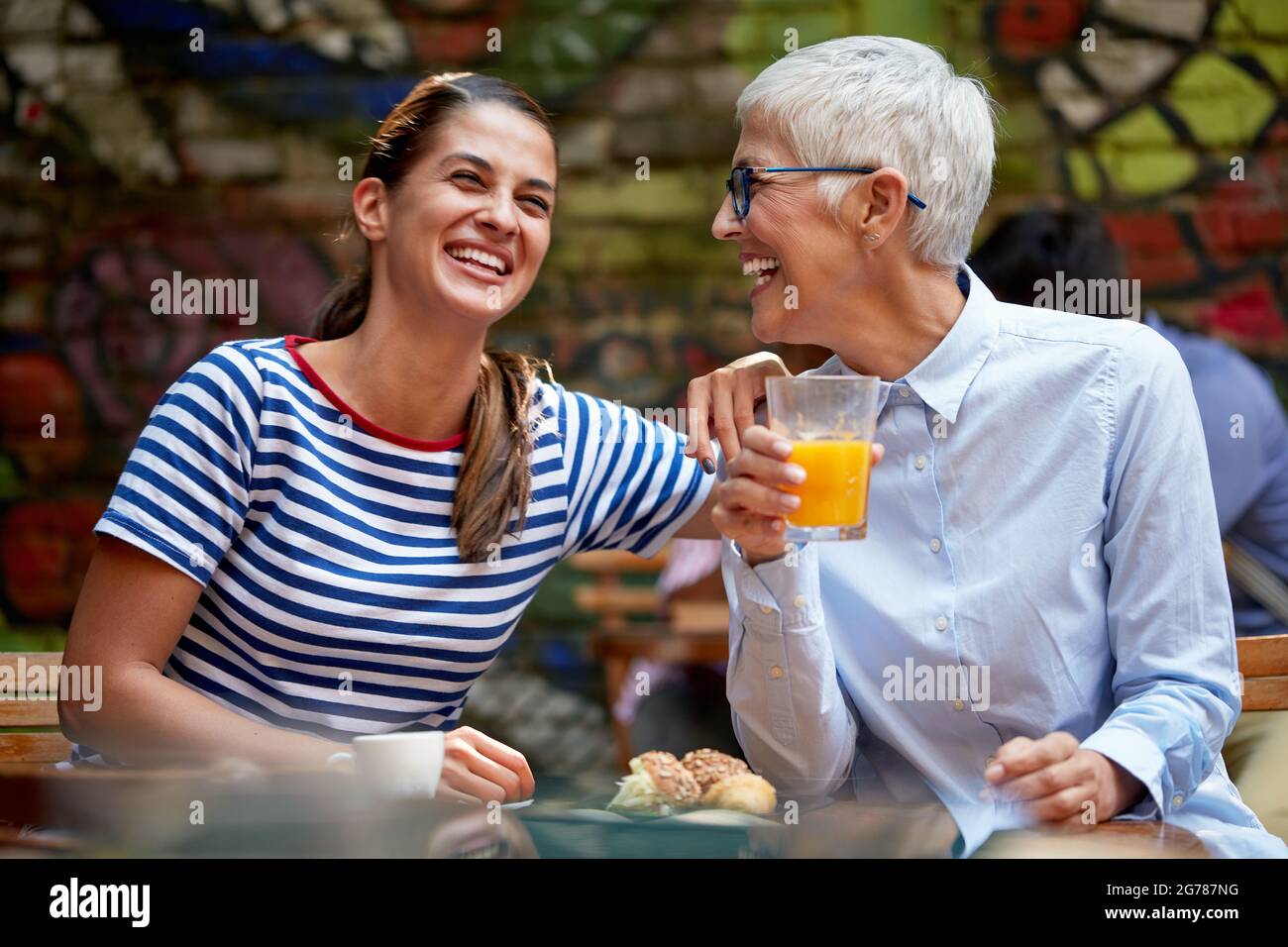 Weibliche Freunde oder Erwachsene Tochter und Mutter Konzept. Junge Frau lachen laut mit älteren kaukasischen Frau, sitzen im Café im Freien. Stockfoto