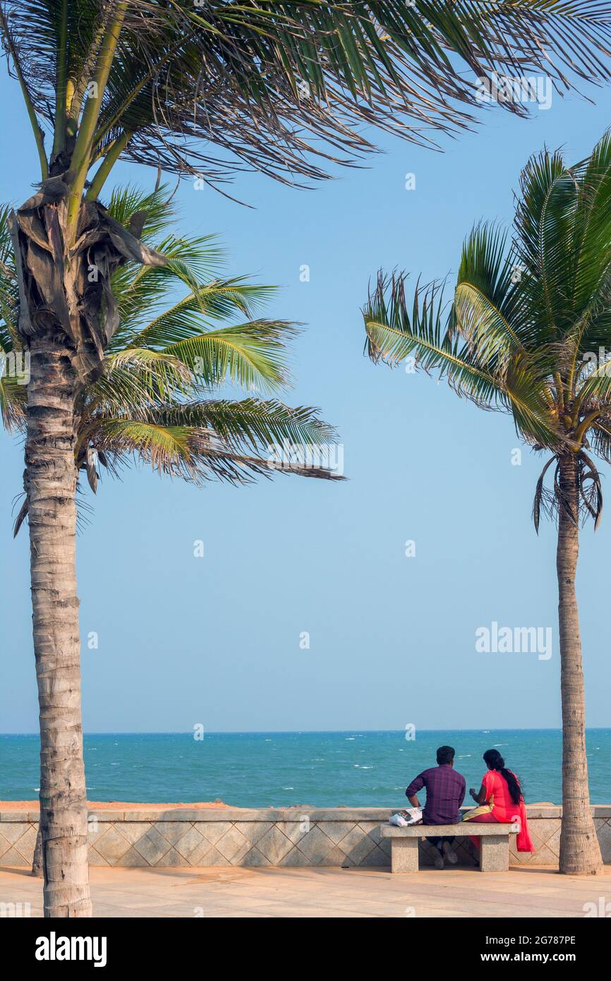 Indisches Paar, das an der Promenade unter Palmen mit Blick auf blaues Meer und blauen Himmel sitzt, Puducherry (Pondicherry), Tamil Nadu, Indien Stockfoto