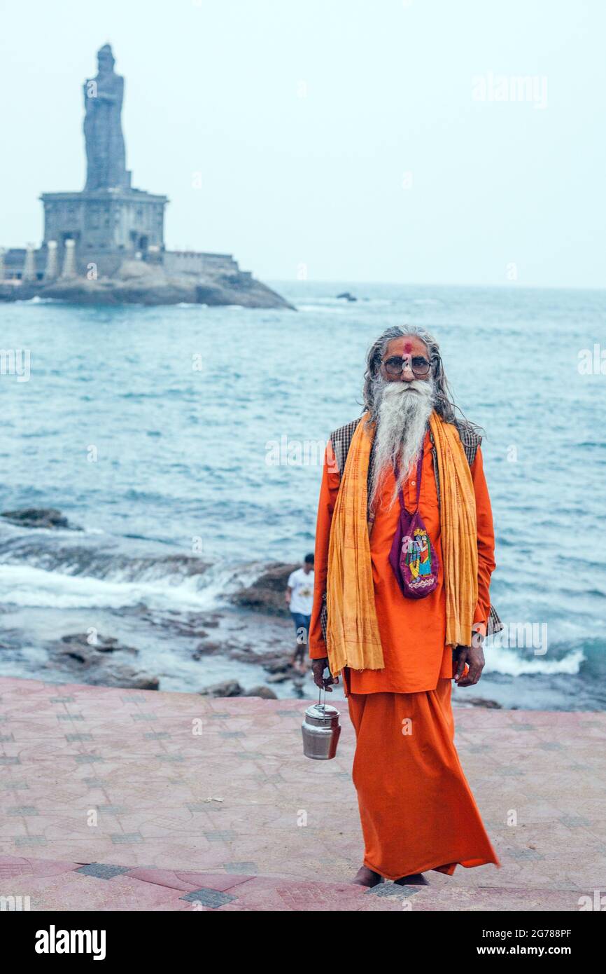 Ältere Hindu-Sadhu mit langen Haaren und Bart posiert in orangefarbenen Gewändern an der Thiruvalluvar Statue, Kanyakumari, Tamil Nadu, Indien Stockfoto