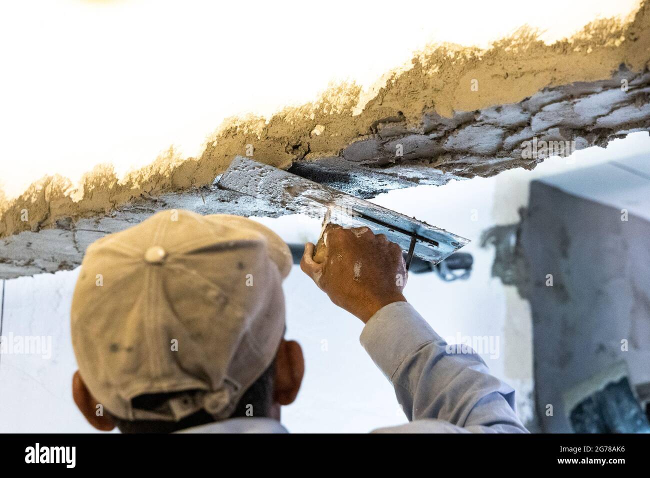 Arbeiter verputzt Zementmörtel auf Betondeckenbalken mit Kelle Stockfoto