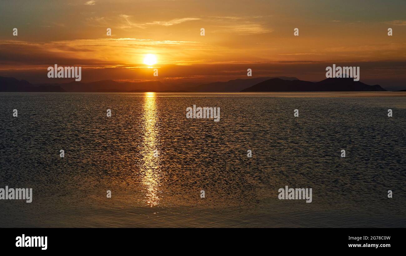 Ionische Inseln, Ithaca, Insel Odysseus, Frikes, Sonnenaufgang, Morgenlicht, Morgenstimmung, Sonne geht über dem Festland auf, Sonnenstrahl auf dem Meer, himmelblau bis orange, leichte Wolkendecke Stockfoto