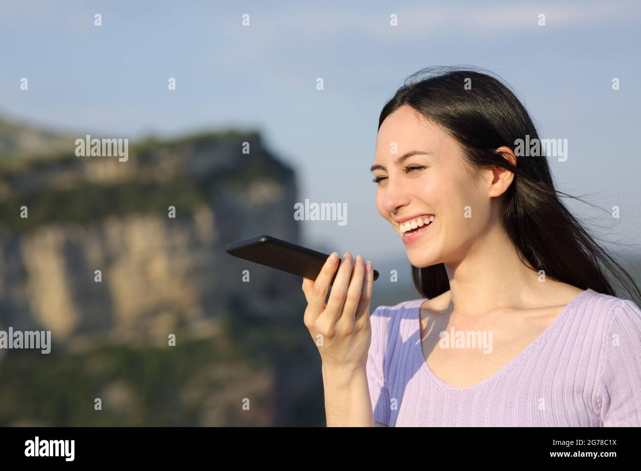 Glückliche asiatische Frau lächelt mit Spracherkennung auf Handy in der Natur Stockfoto