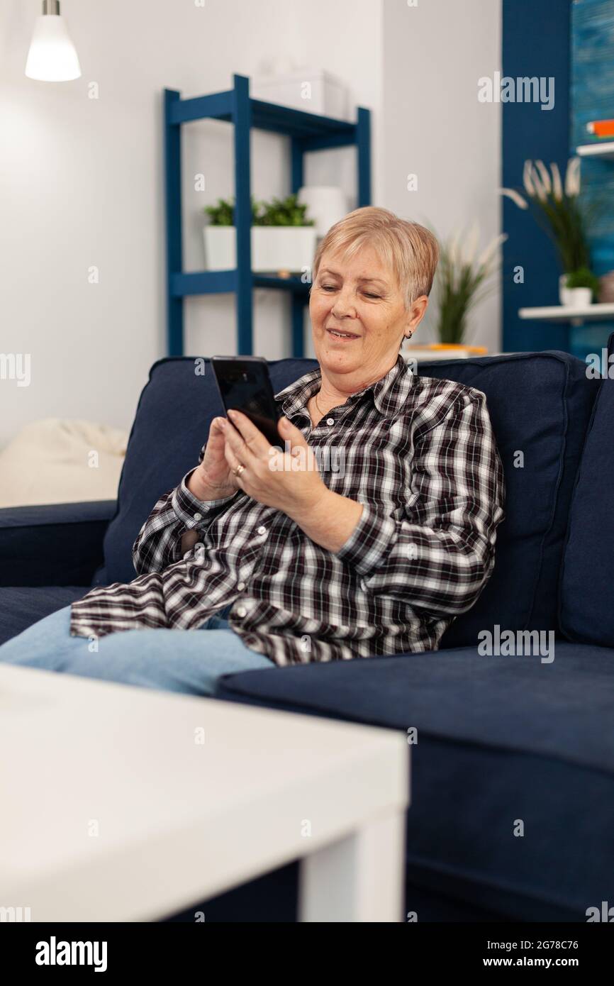 Hapy ältere Dame SMS am Telefon entspannen auf dem Sofa genießen Ruhestand Lebensstil. Ältere Frau im Internet surfen mit Smartphone sitzen auf dem Sofa im Wohnzimmer zu Hause. Stockfoto