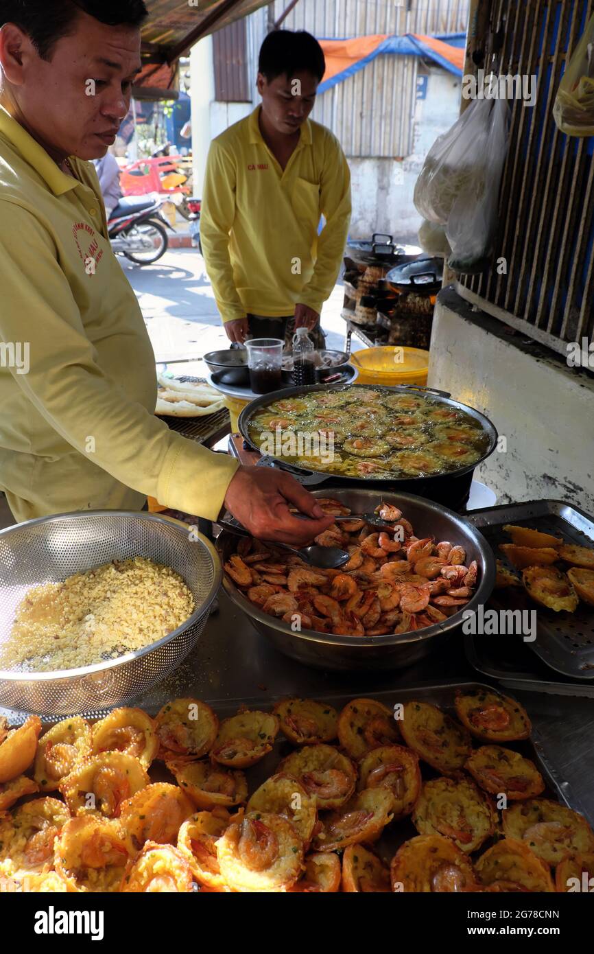 HO-CHI-MINH-STADT, VIET NAM- 5. JANUAR 2020: Zwei vietnamesische Männer, die Mini-Shrimp-Pfannkuchen auf dem Bürgersteig im Restaurant, gelbe knusprige Kuchen in Kochtöpfen machen Stockfoto