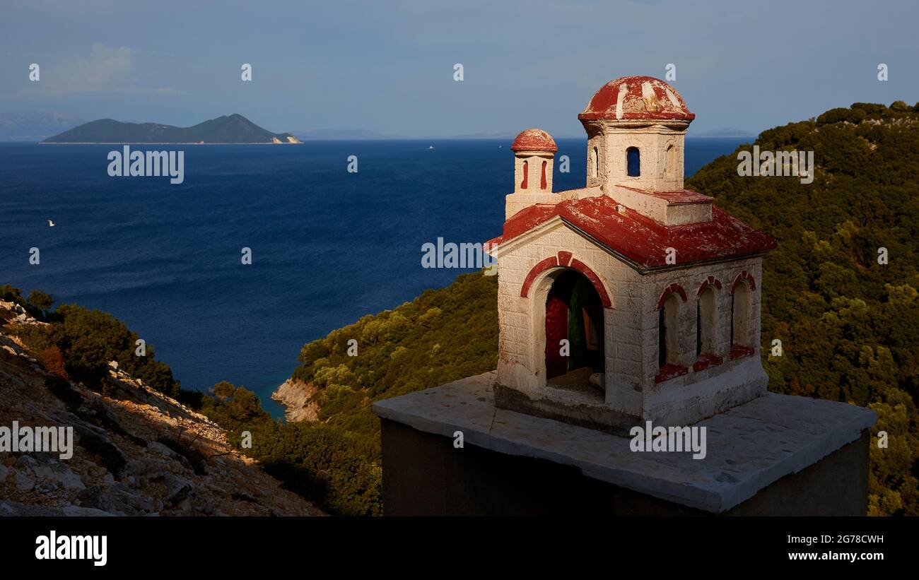 Ionische Inseln, Ithaca, Insel Ulysses, Nordostküste, Bucht von Marmakas, Die Insel Atokos ist im Hintergrund links zu sehen, eine Miniaturkapelle an der Straße rechts, das Meer ist dunkelblau, der Himmel hellblau Stockfoto