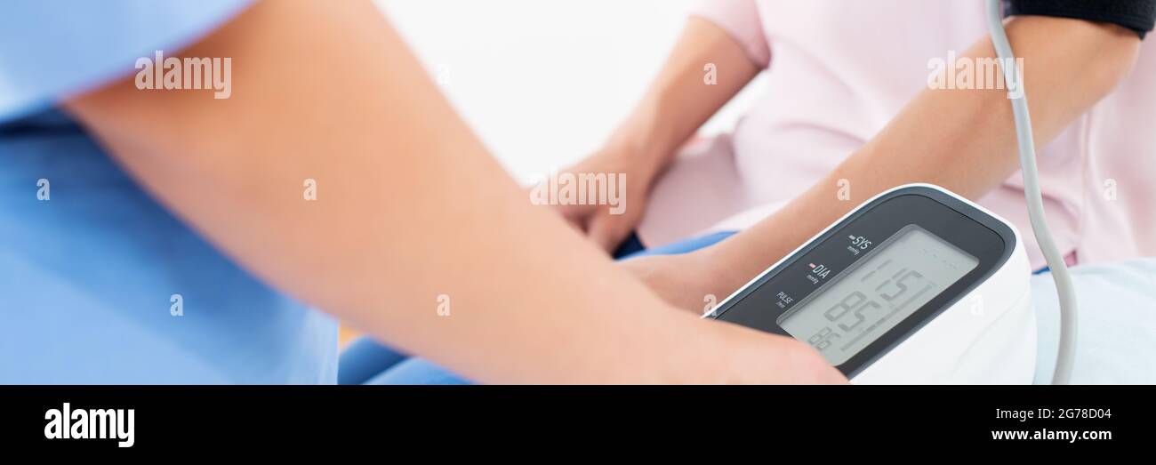 Die junge Frau lässt ihren Blutdruck von einer Krankenschwester, einem Arzt oder einem Gesundheitsgast überprüfen. Banner zur Herzgesundheit. Digitaler Blutdruckmessgerät. Stockfoto