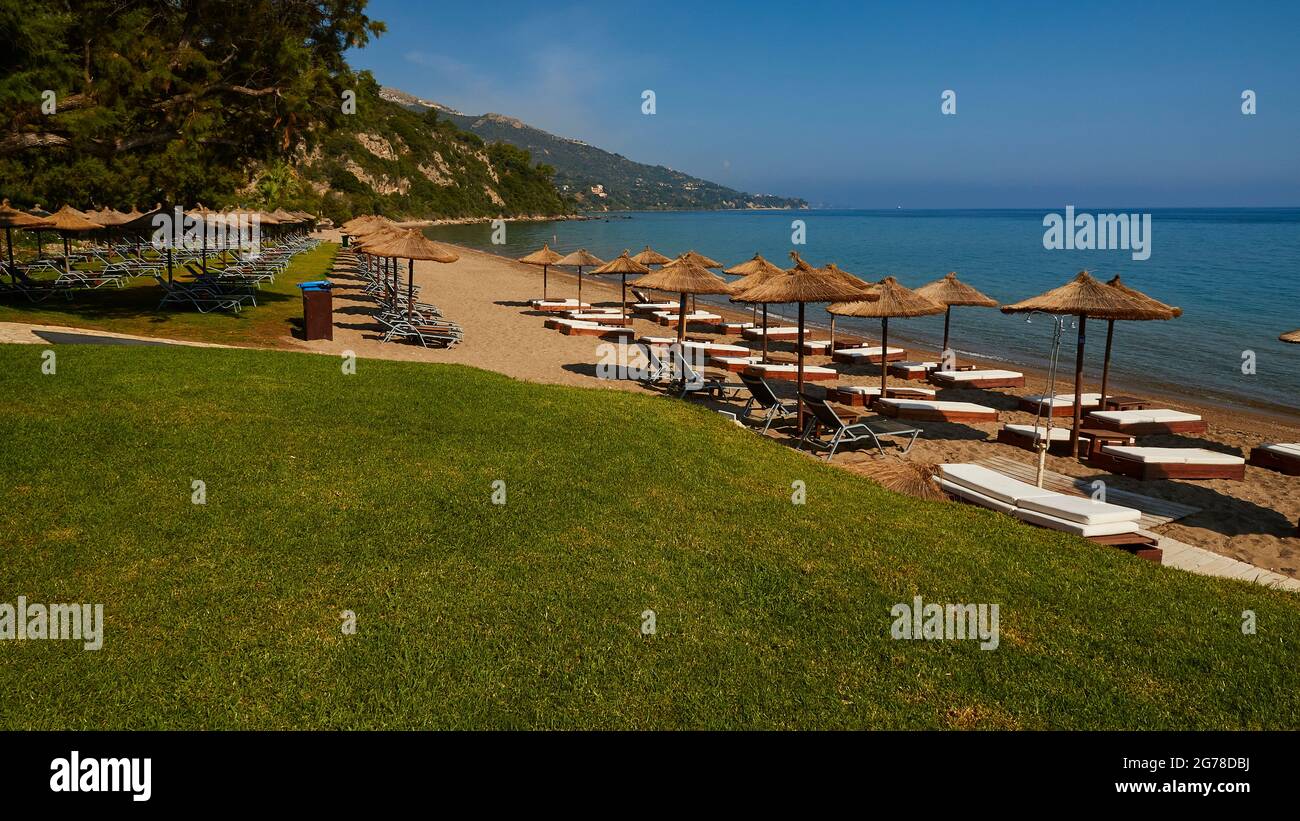 Ionische Inseln, Zakynthos, südlich der Stadt Zakynthos, Banana Beach, grüner Rasen, hinter Sonnenschirmen und Sonnenliegen, keine Menschen, blaues Wasser, blauer Himmel Stockfoto