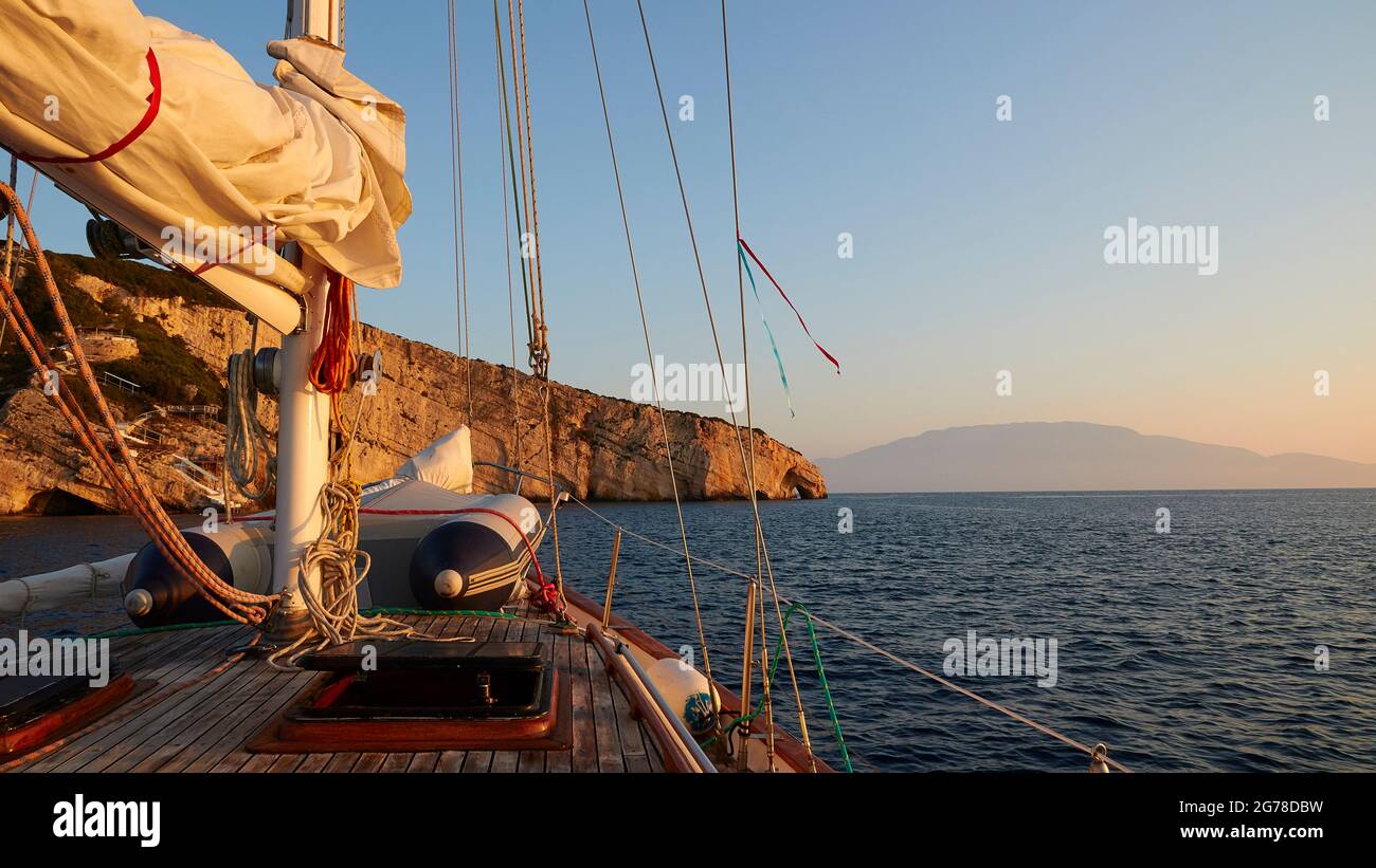 Ionische Inseln, Zakynthos, Nordostküste, Blaue Höhlen, Blaue Grotten, Morgenlicht, Blick vom Segelboot auf die Blauen Grotten, Takelage, Sonnenglühen, dunkles Meer, hellblauer Himmel, Berg auf dem Festland im Morgennebel Stockfoto