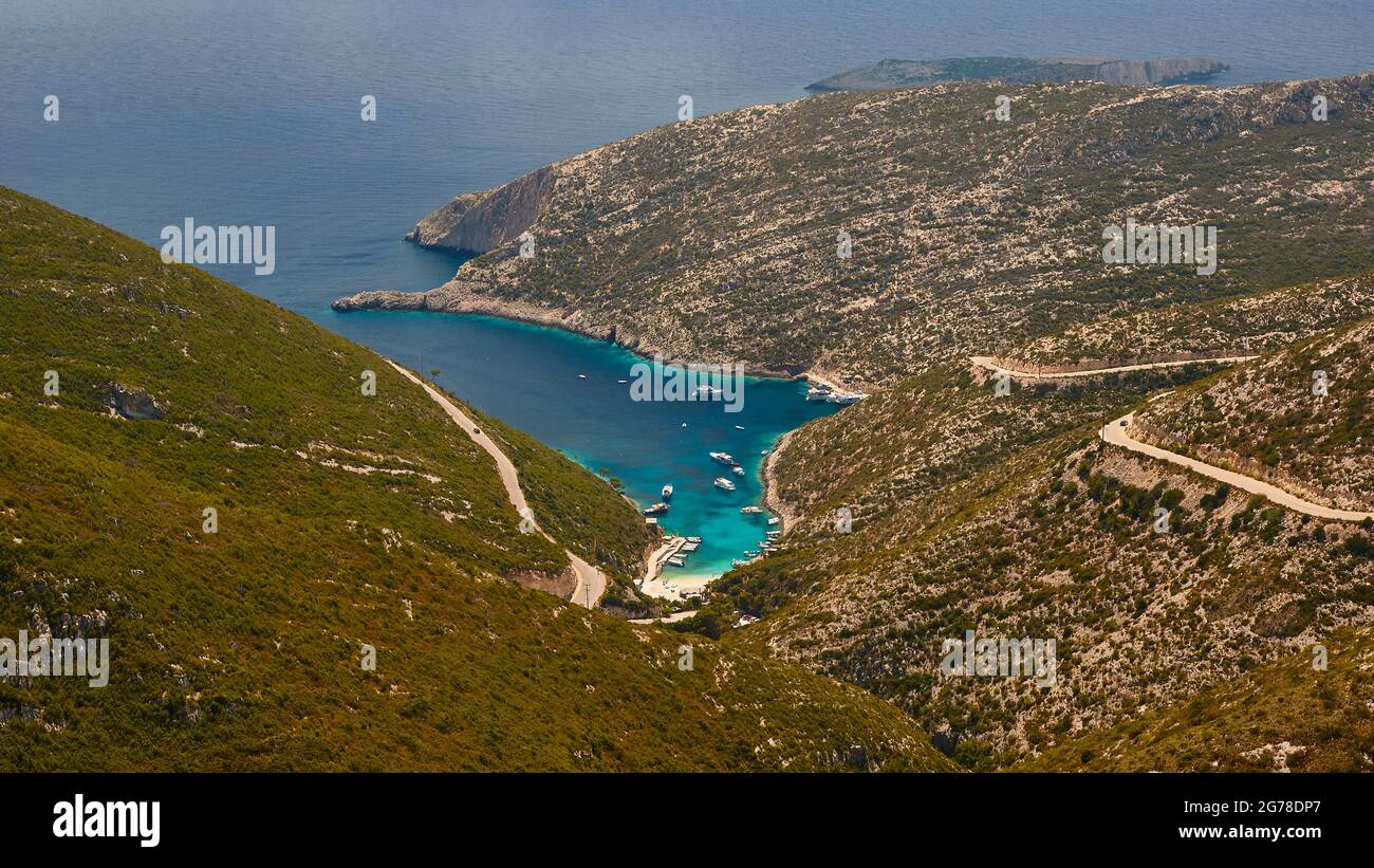 Ionische Inseln, Zakynthos, Westküste, Adria, Strand, Hafen, Porto Vromi, Panoramablick von weit oben, tiefe Einbuchtung der Bucht, blaues, grünes und türkisfarbenes Wasser in der Bucht, Meerwasser graublau im Hintergrund, bewachsene Hügel links von der Bucht, dünn bewachsene Hügel mit der Straße rechts über der Bucht Stockfoto