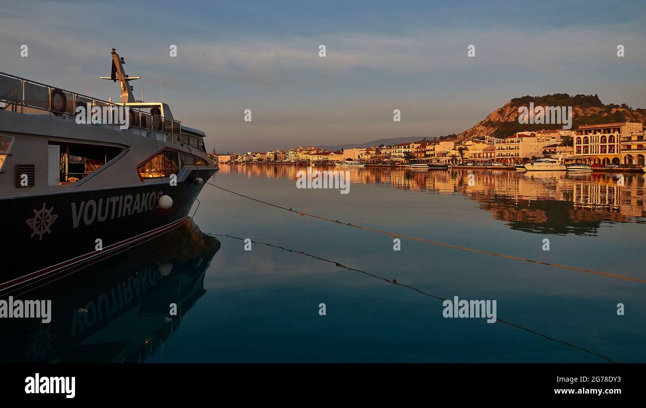 Zakynthos, Zakynthos Stadt, Morgenlicht, Hafen, Ausflugsboot im Bild im Schatten, spiegelglattes, dunkelblaues Meer in der Mitte, morgendliche Skyline von Zakynthos Stadt und Burghügel Stockfoto
