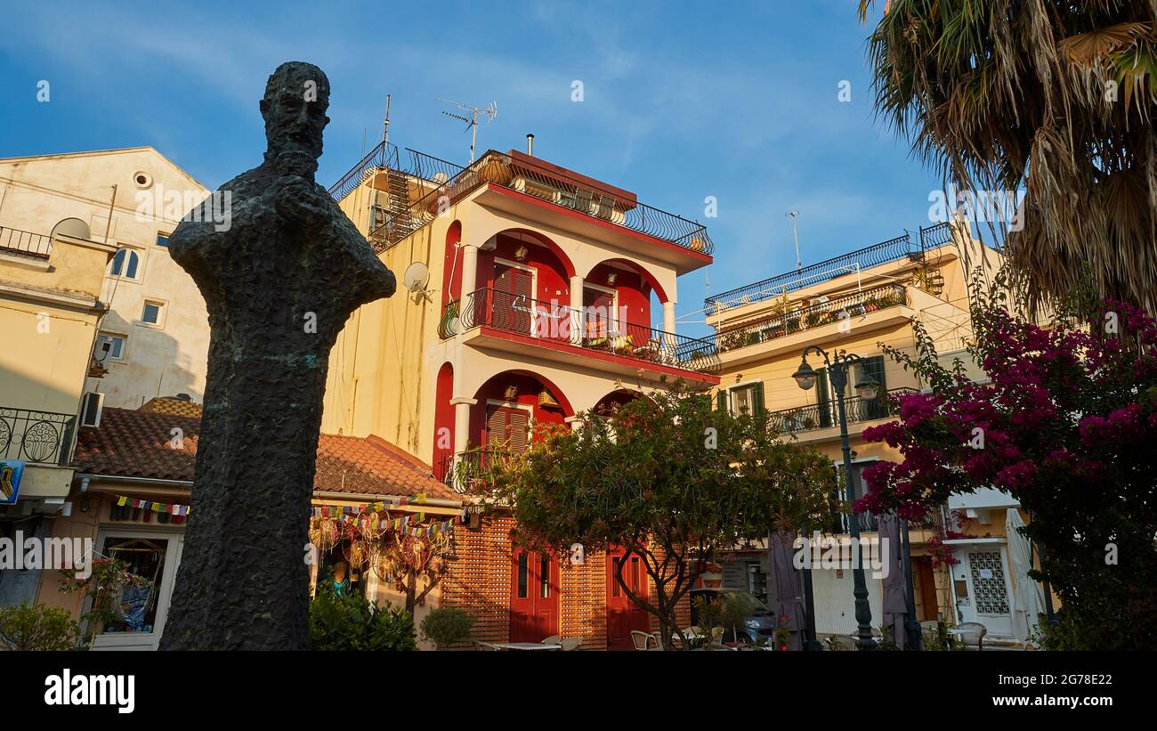 Zakynthos, Zakynthos Stadt, Stadtzentrum, Gebäude, Morgenlicht, Statue des Mönchs Anthimos Argyropoulos, im Schatten, dahinter Gebäude im Morgenlicht, blauer Himmel mit wispigen Wolken Stockfoto