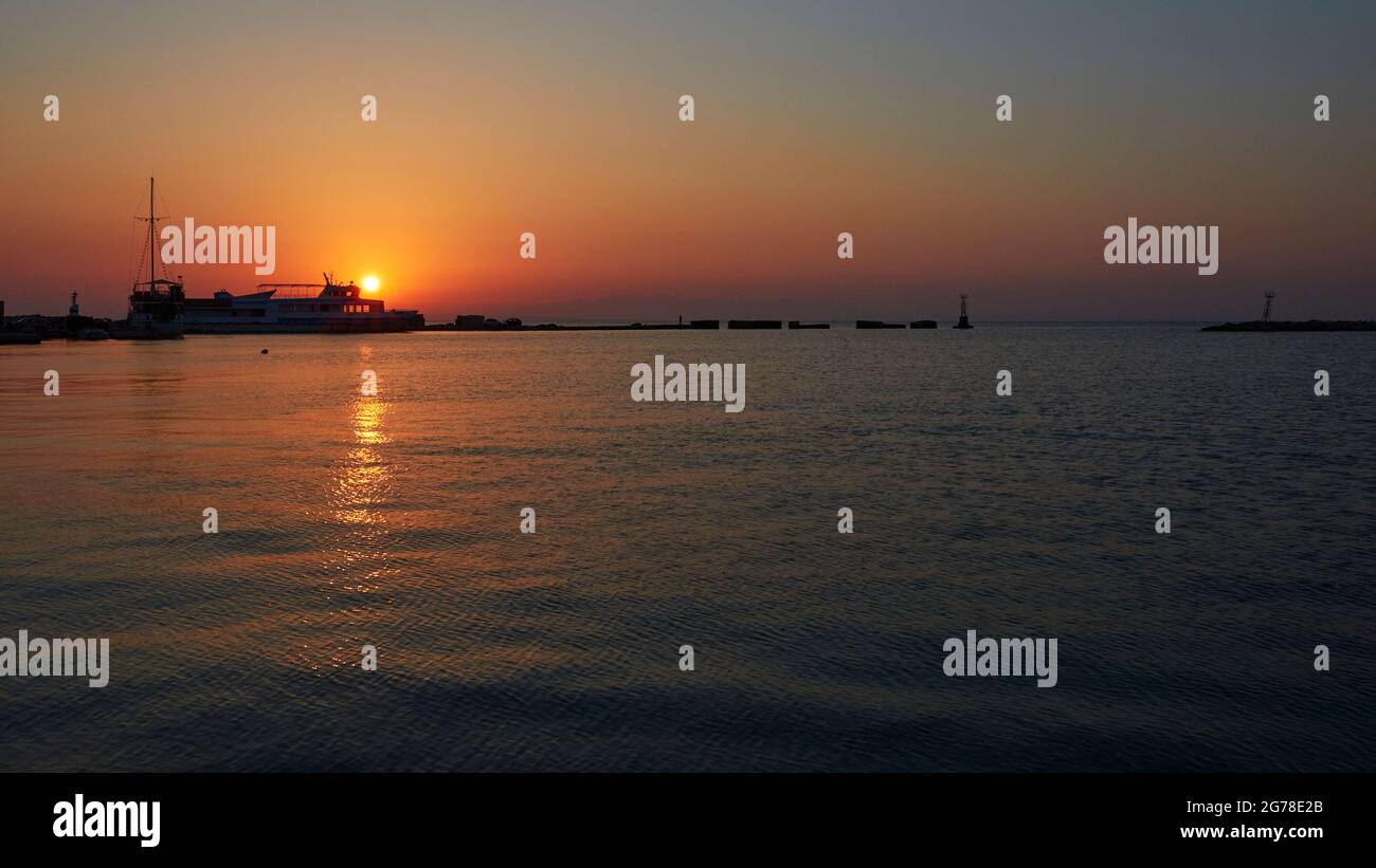 Zakynthos, Zakynthos Stadt, Hafen, Sonnenaufgang, unteres 2/3 Wasser dunkelblau mit Sonnenreflexion, Himmel am oberen dritten Morgen orange-rot-blau, aufgehende Sonne klein hinter Ausflugsboot, Hafeneingang Stockfoto