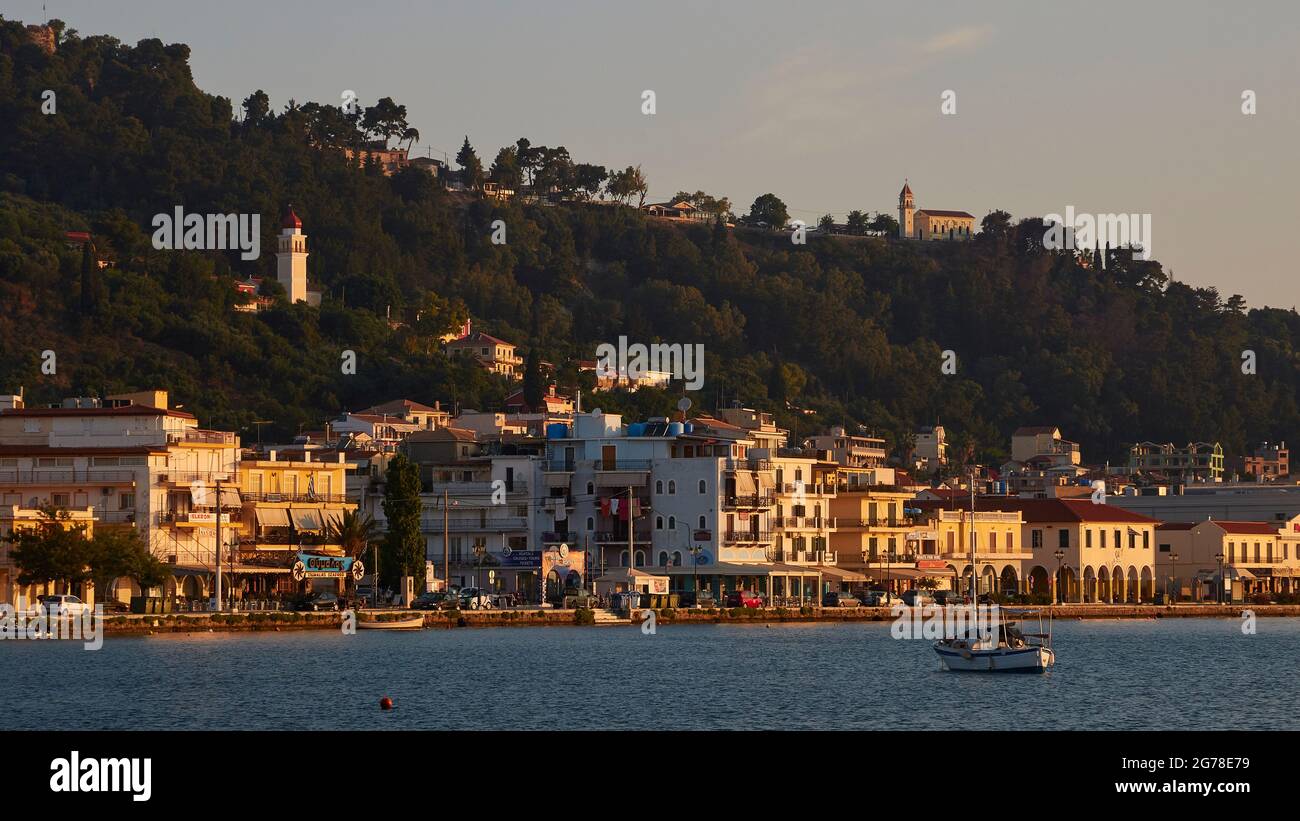 Zakynthos, Zakynthos City, Morgenlicht, Teilansicht der Skyline von Zakynthos City, von Südosten aus über das Meer gesehen, Boot im Vordergrund, Panagia Pikridiotissa Kirche links im Bild, Agia Paraskevi Kirche oben rechts auf einem Hügel Stockfoto