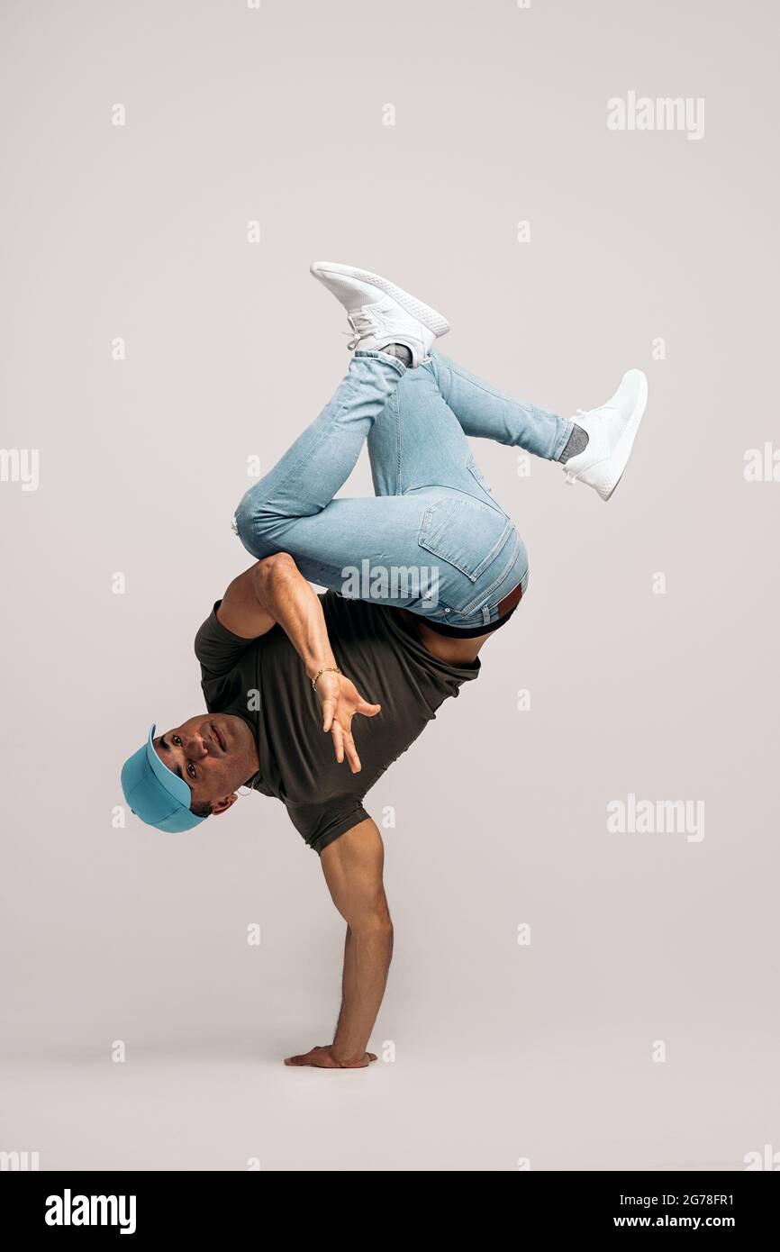 Hispanische Tänzerin mit legerer Kleidung, die Handstand macht und im Studio vor weißem Hintergrund tanzt. Stockfoto