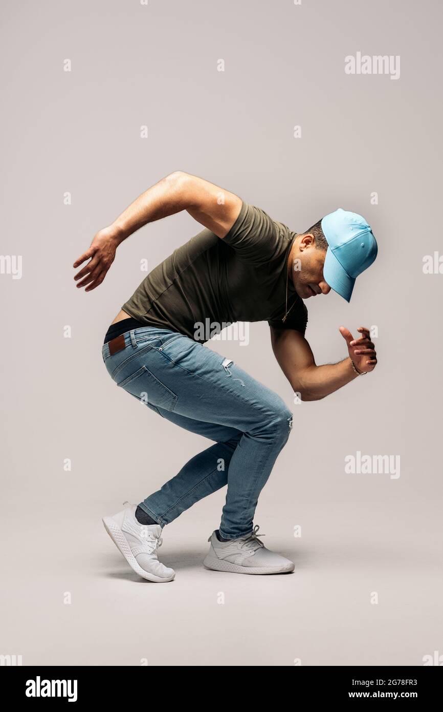 Unerkannte lateinische Tänzerin mit Hut und Spaß im Studio vor weißem Hintergrund mit Hip-Hop-Moves. Stockfoto