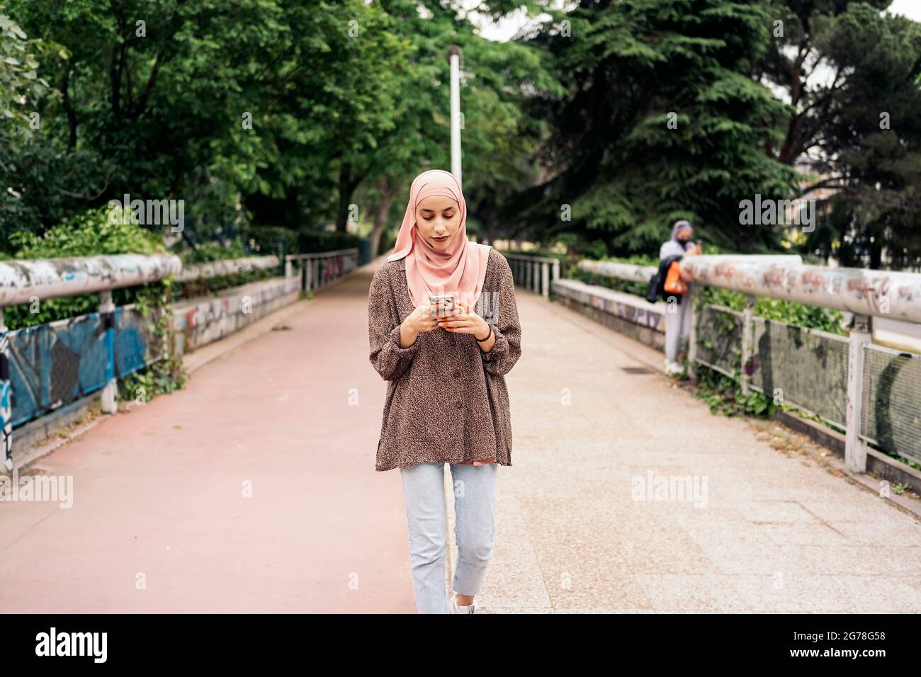 Schönes muslimisches Mädchen, das im Park läuft und ihr Smartphone eintippt. Stockfoto