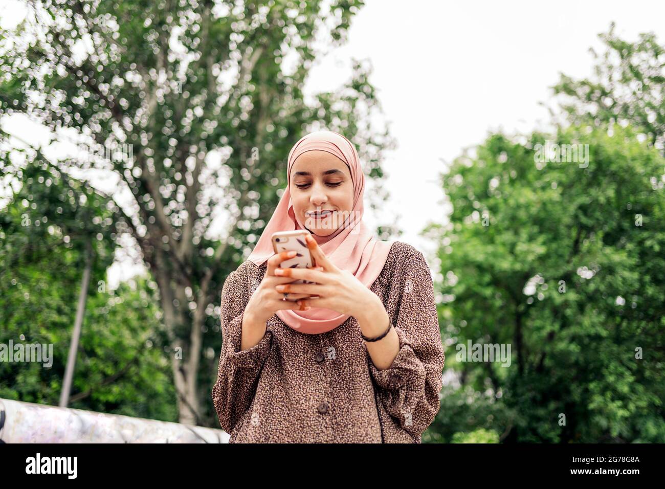 Hübsches muslimisches Mädchen, das im Park läuft und ihr Handy eintippt. Stockfoto