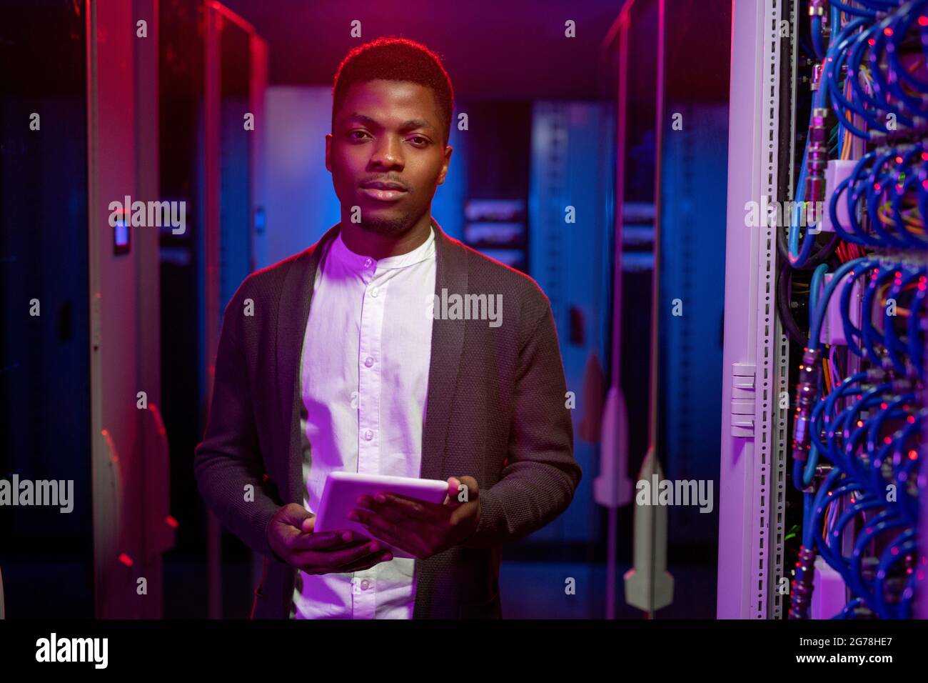 Porträt eines selbstbewussten, gutaussehenden jungen afroamerikanischen Mannes, der für die Verwaltung des Netzwerksystems verantwortlich ist und mit einem Tablet im Rechenzentrum steht Stockfoto