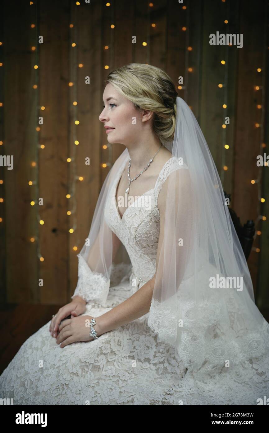 Braut in einem elfenbeinfarbenen Hochzeitskleid mit einem Schleier mit Spitze und einem großen Blumenstrauß in Pastelltönen. Stockfoto