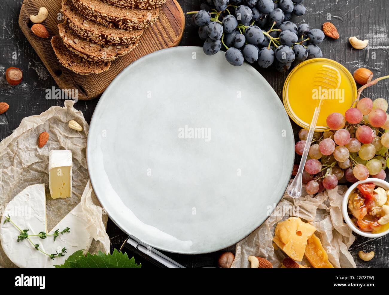 Leerer Mockup-Teller auf dem Abundance-Tisch mit Lebensmitteln. Mockup Teller serviert in Rahmen von Lebensmitteln für Gourmet-Abendessen Produkte Brot Käse Honig Trauben Stockfoto