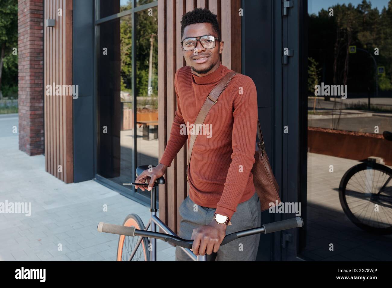 Junger Mann afrikanischer Herkunft mit Fahrrad, der vor der Kamera steht Stockfoto