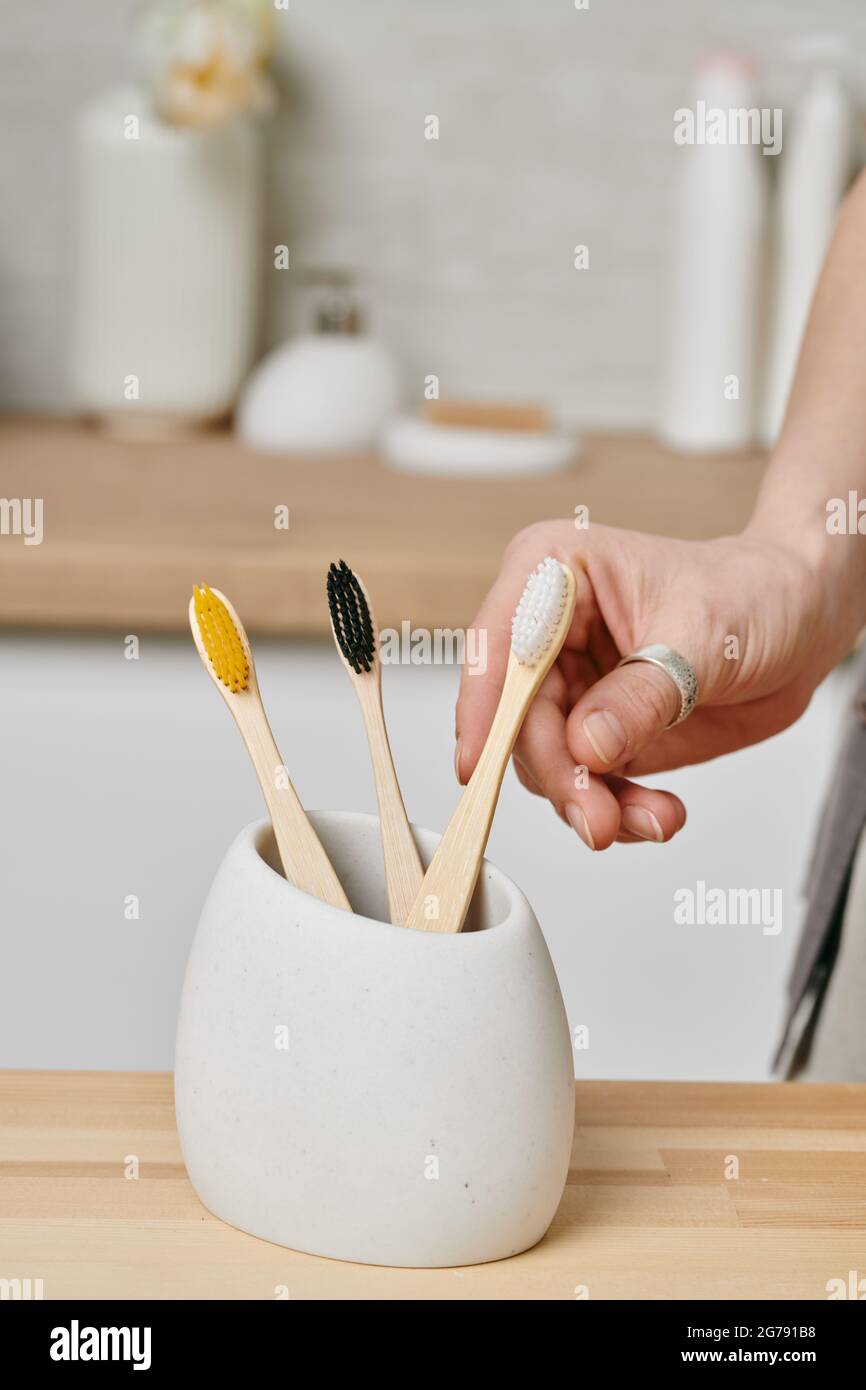 Die Hand einer Frau nimmt die Zahnbürste aus der weißen Schüssel auf dem Holztisch Stockfoto