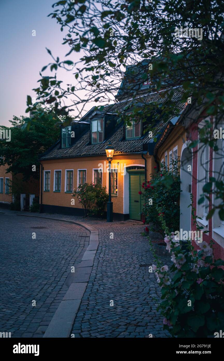 Gelbes Häuschen mit Blumen entlang der Kopfsteinpflasterstraße in Lund Schweden in der Sommernacht Stockfoto