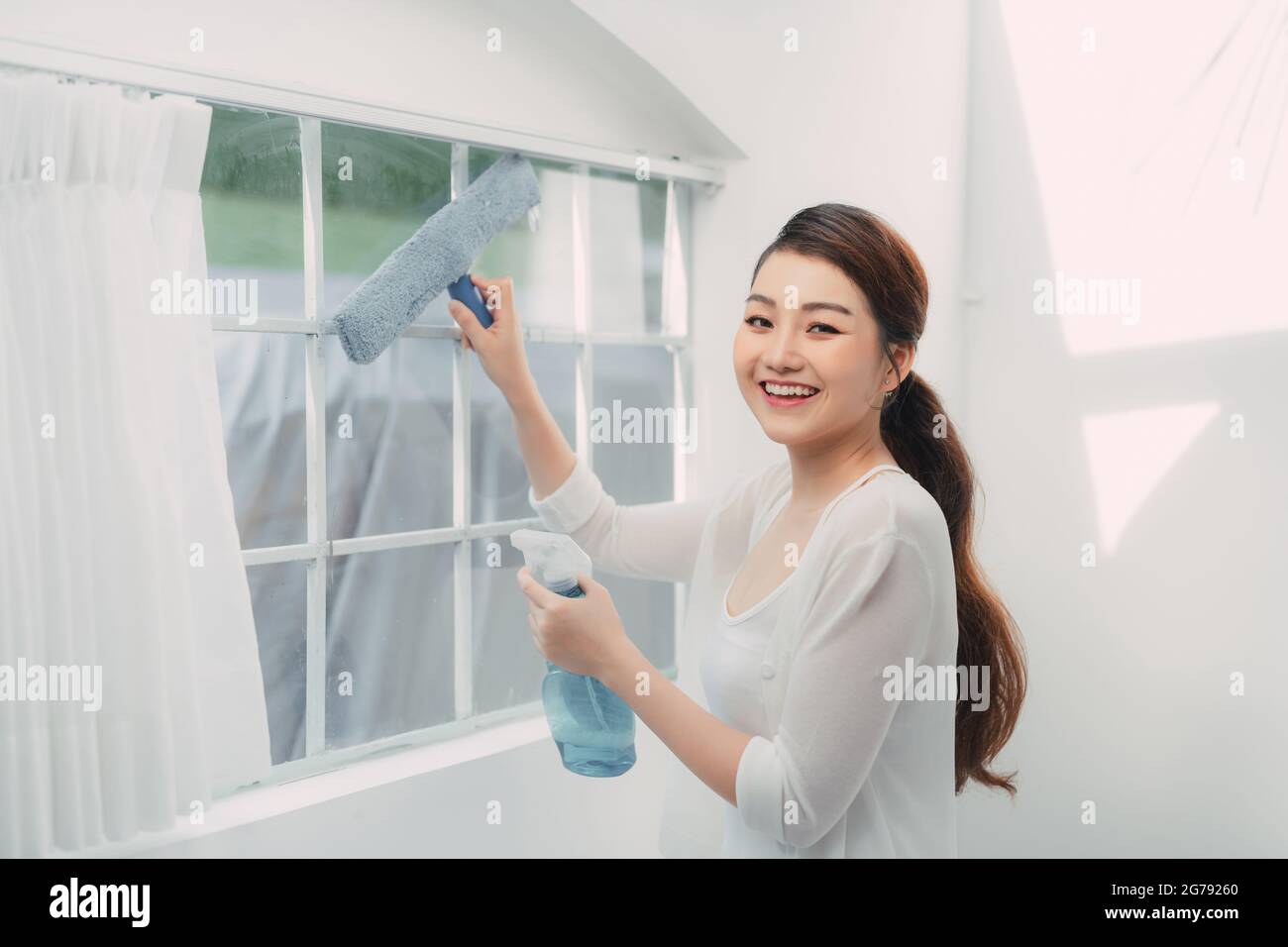 Junge lächelnde Frau putzt Fenster in einem Haus, macht Hausarbeiten. Stockfoto