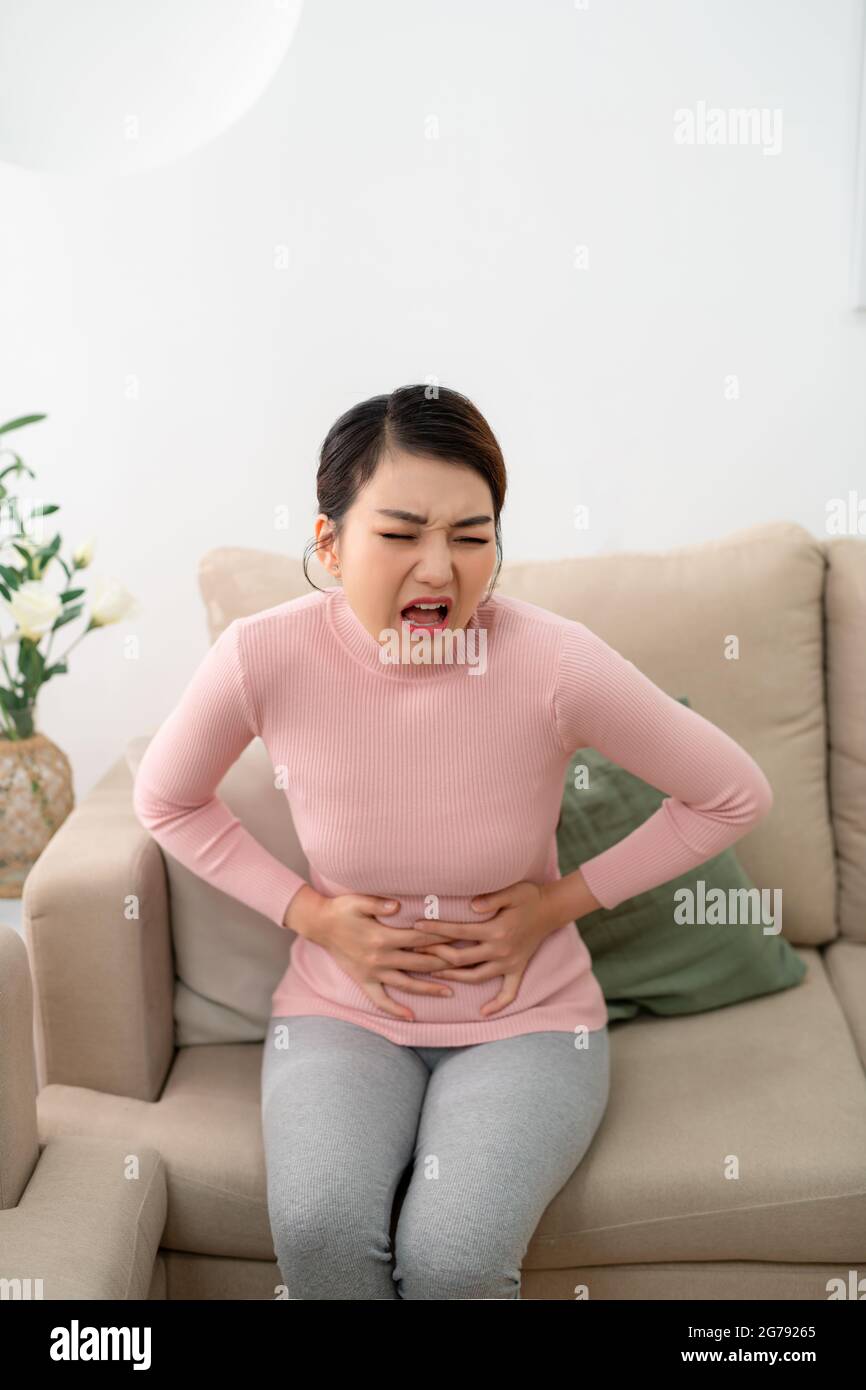 Junge Frau mit Bauchschmerzen, während sie zu Hause auf dem Sofa sitzt Stockfoto