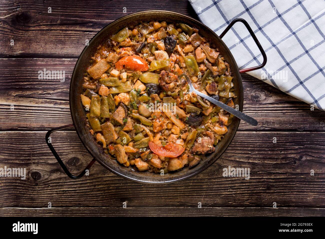 Paella mit Gemüse auf einem Holztisch, traditionelles Essen, Löffel, Familienessen Stockfoto