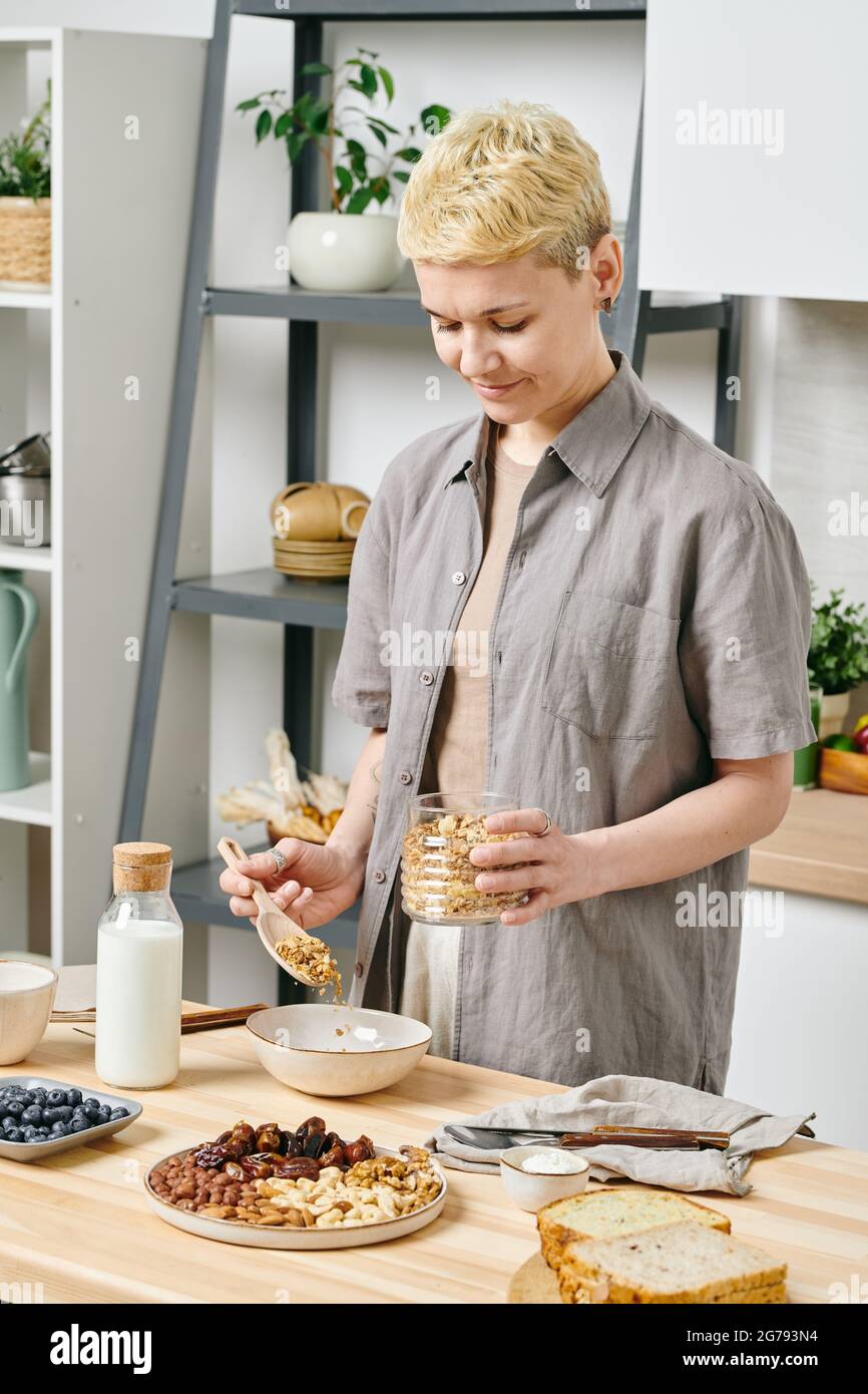 Gesunde junge Frau, die am Küchentisch Müsli zubereitet Stockfoto