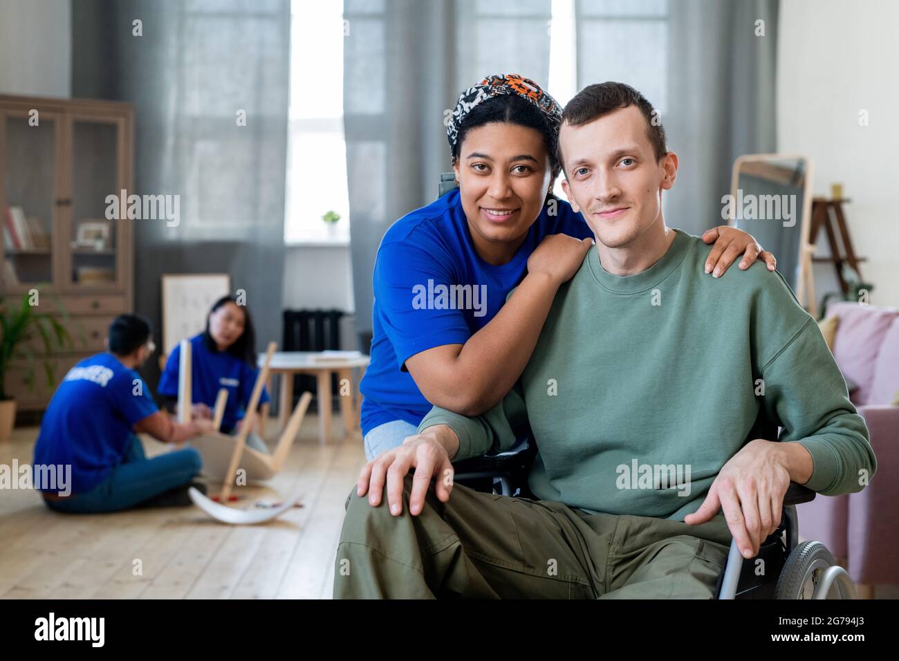 Glückliche junge Mischrasse weibliche Freiwillige umarmt behinderten Mann im Rollstuhl Stockfoto