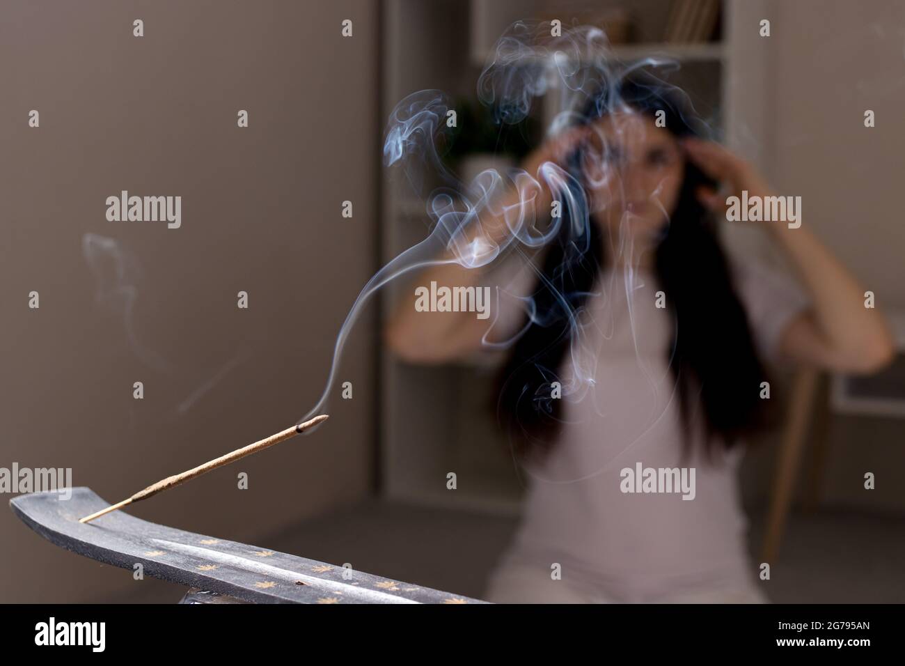 Ein aromatischer Indianerstab brennt, die Frau im Hintergrund meditiert. Aromatherapie, Selbsteintauchen, die Kraft des Denkens Stockfoto