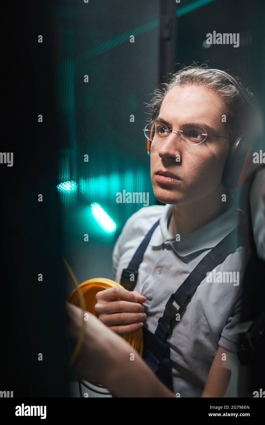 Vertikales Porträt eines jungen Netzwerktechnikers, der während der Wartungsarbeiten im Rechenzentrum Kabel im Serverraum anführt Stockfoto
