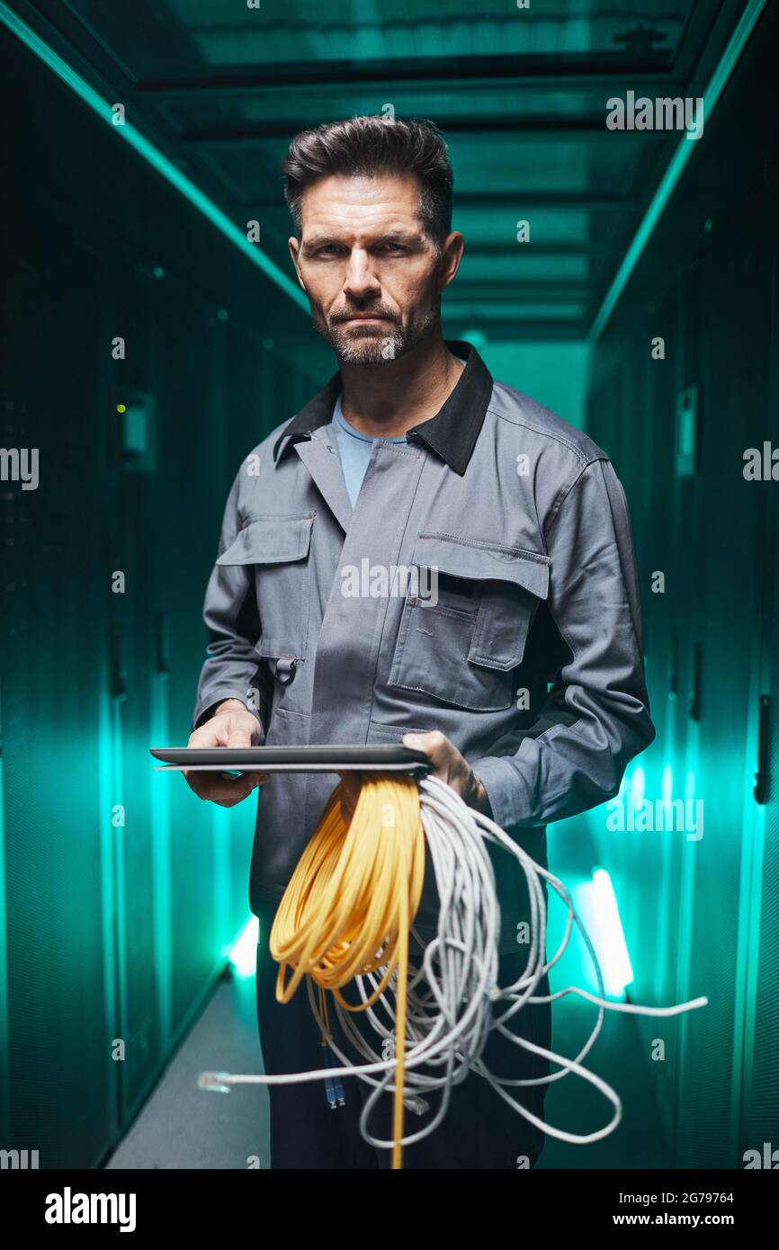 Vertikales Porträt eines ausgereiften Netzwerktechnikers, der während der Wartungsarbeiten im Rechenzentrum ein digitales Tablet im Serverraum verwendet Stockfoto