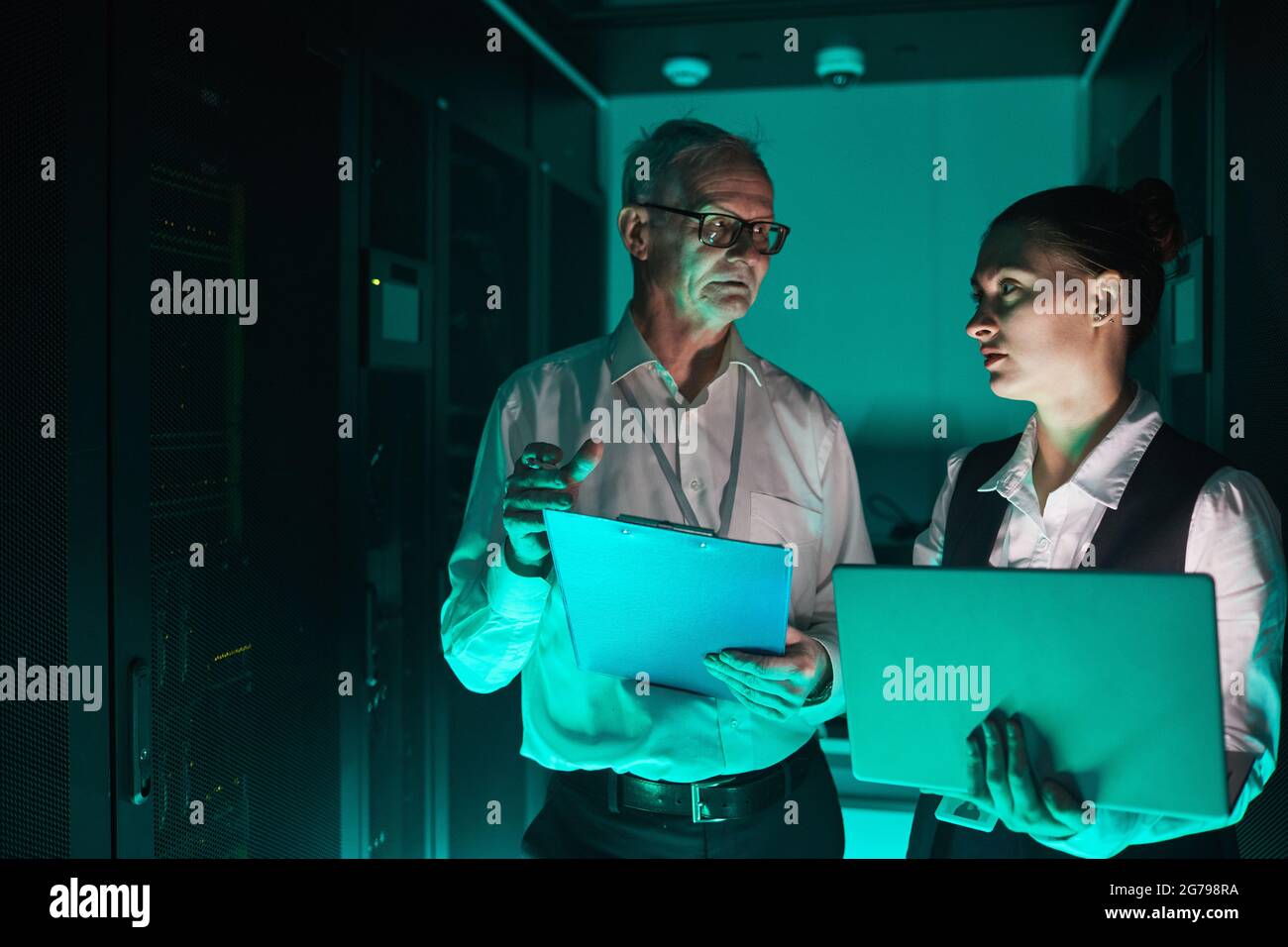 Futuristisches Porträt von zwei Data Scientists, die im Serverraum einen Laptop verwenden, während sie mit Supercomputer und Kopierraum arbeiten Stockfoto