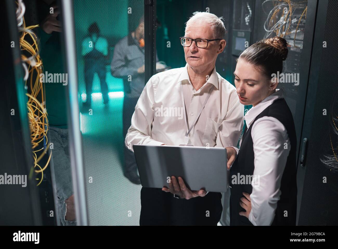 High-Angle-Ansicht von zwei Data Scientists, die mit einem Laptop arbeiten, während sie mit Supercomputern im Rechenzentrum arbeiten, Speicherplatz kopieren Stockfoto