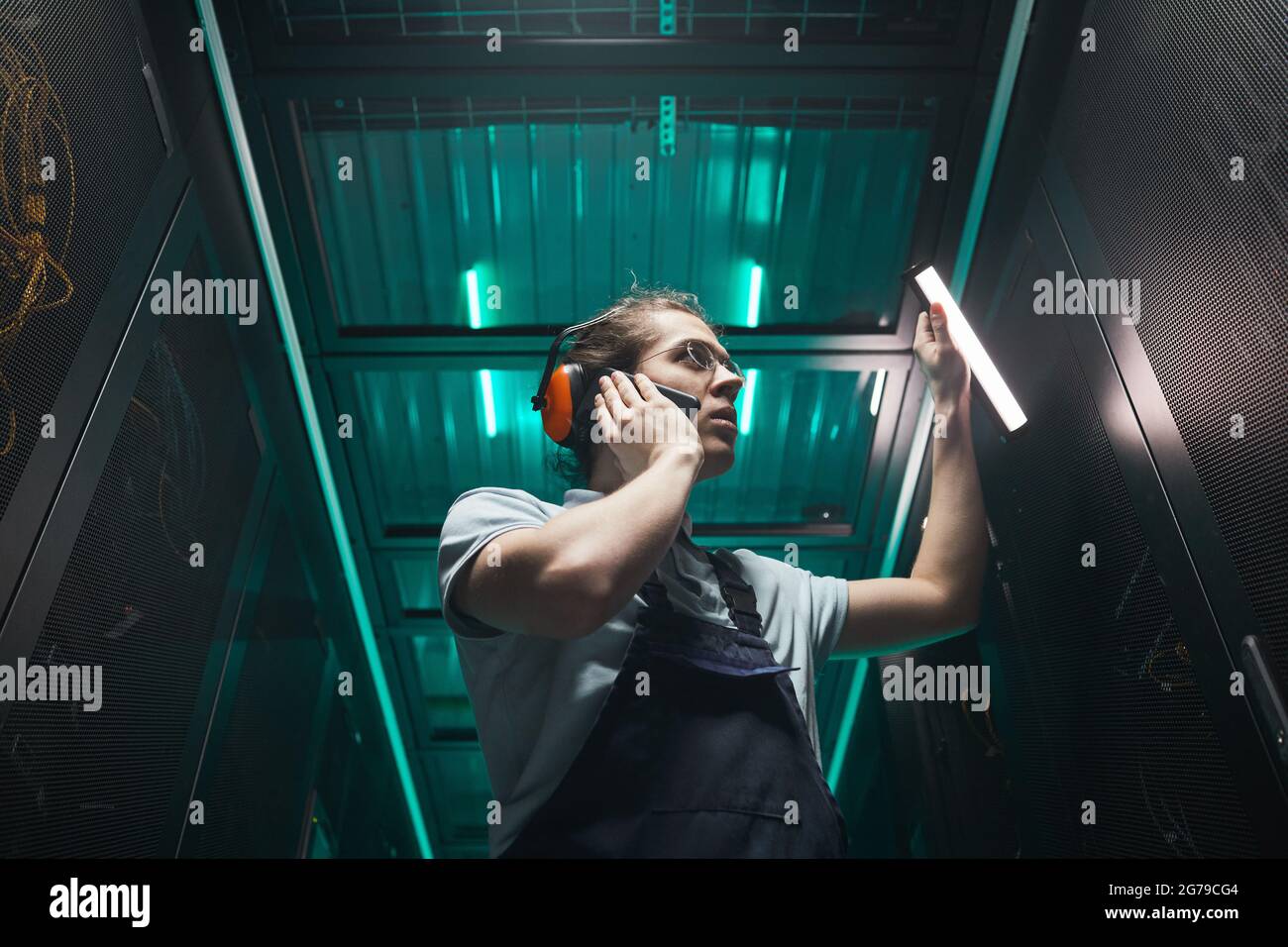 Porträt eines männlichen Netzwerktechnikers, der mit dem Smartphone im Serverraum spricht, während er im Rechenzentrum arbeitet und Platz kopiert Stockfoto