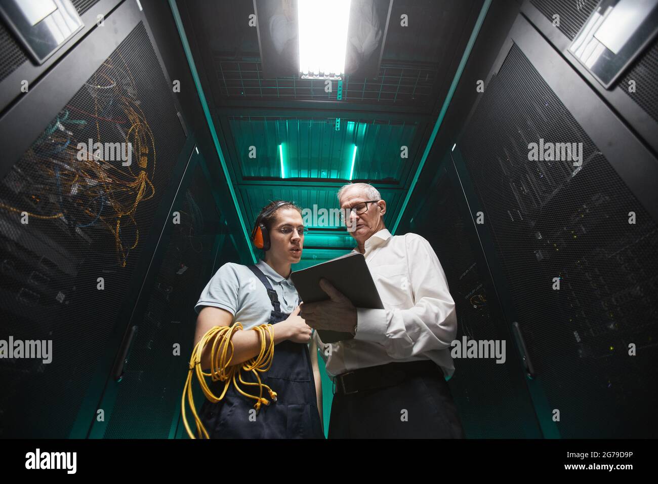 Im niedrigen Winkel porträtiert zwei Techniker, die im Serverraum ein Tablet verwenden, während sie Wartungsarbeiten im Rechenzentrum durchführen und Platz für Kopien verwenden Stockfoto