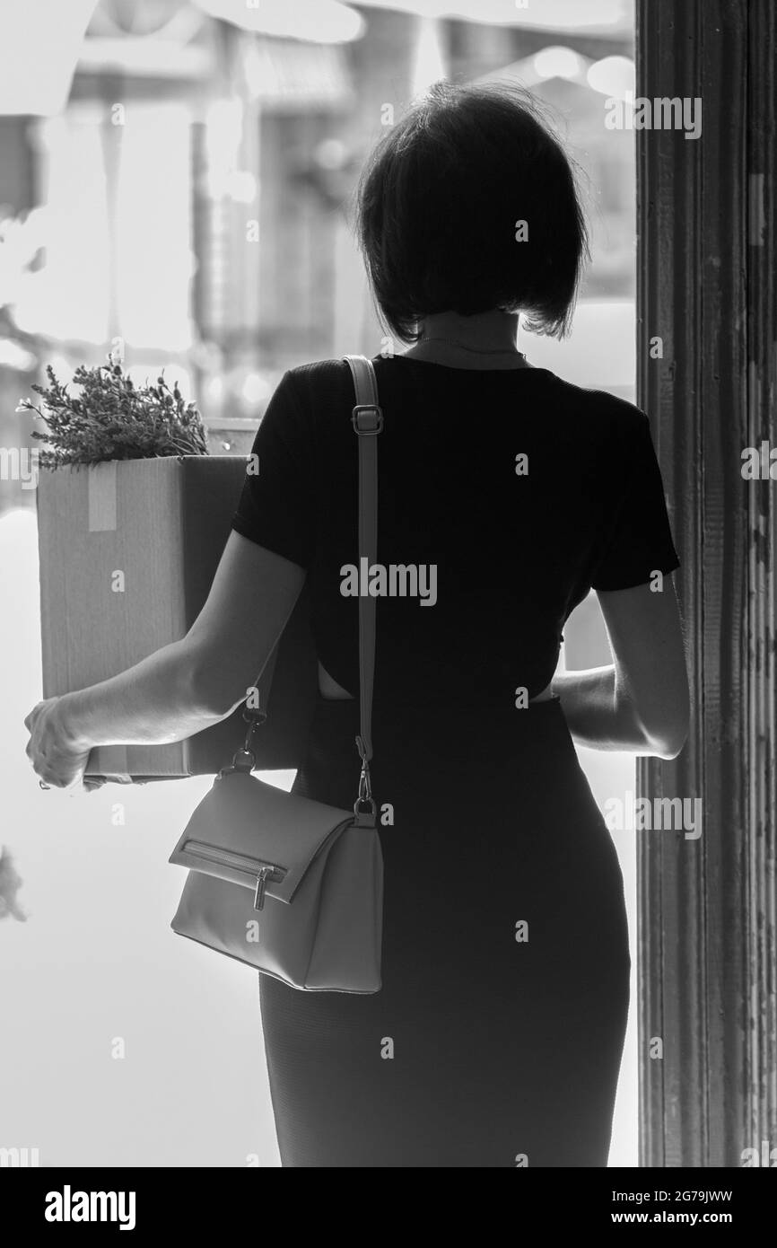 Eine gefeuerte Brünette in einem schwarzen Kleid mit einer Schachtel persönlicher Gegenstände. Schwarz und Weiß Stockfoto