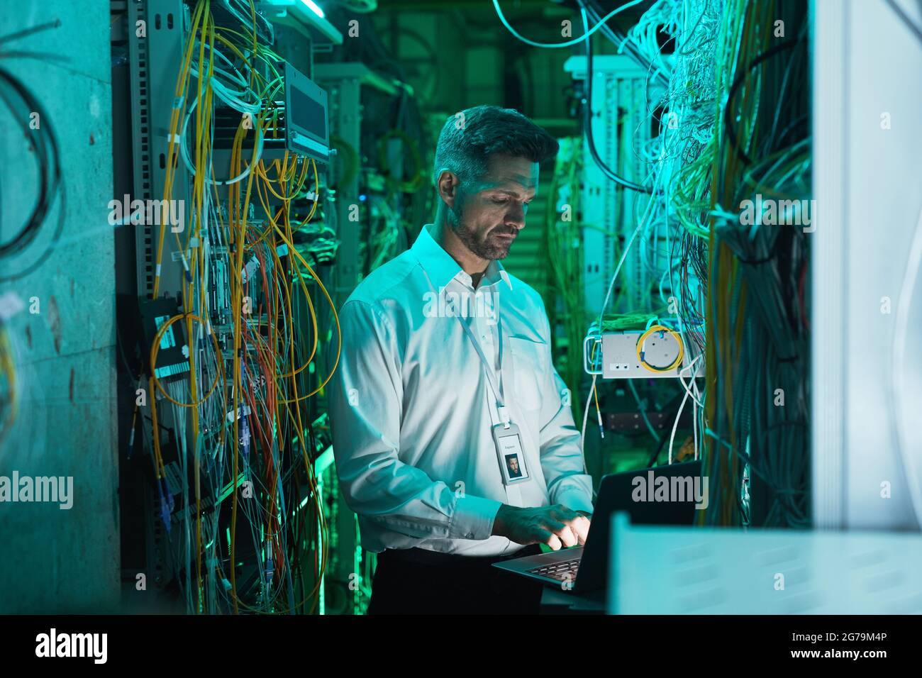 Machen Sie einen reifen Netzwerktechniker mit einem Laptop im Serverraum, während Sie mit einem Supercomputer im Rechenzentrum arbeiten, und kopieren Sie Speicherplatz Stockfoto