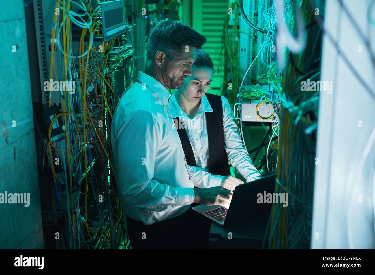 Zwei Netzwerktechniker, die im Serverraum einen Laptop verwenden, während sie mit einem Supercomputer im Rechenzentrum arbeiten, können aus einem hohen Blickwinkel betrachtet werden Stockfoto