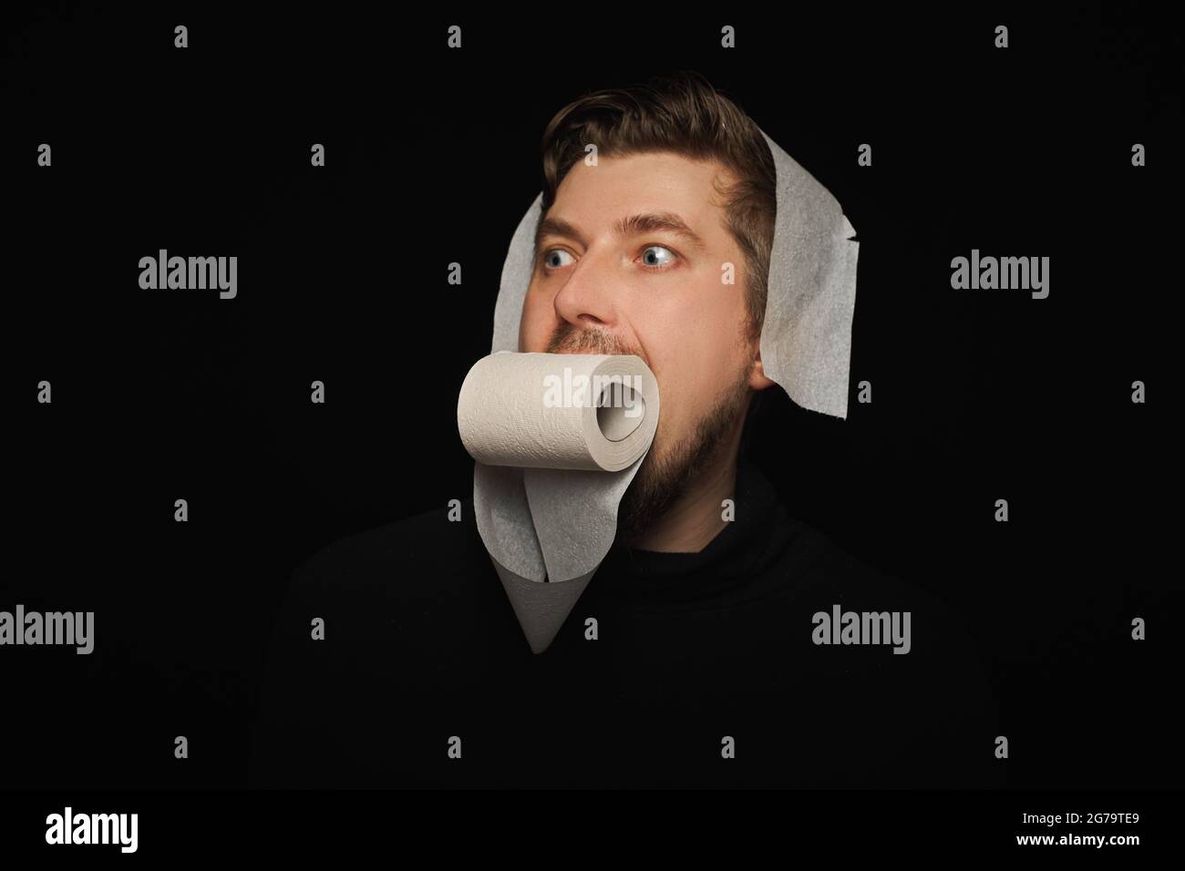 Mann, der Toilettenpapier isst. Lustige Hunger Mann, Fasten Konzept. Hungerstreik. Verrückter bärtiger Kerl. Schwarzer Hintergrund. Stockfoto