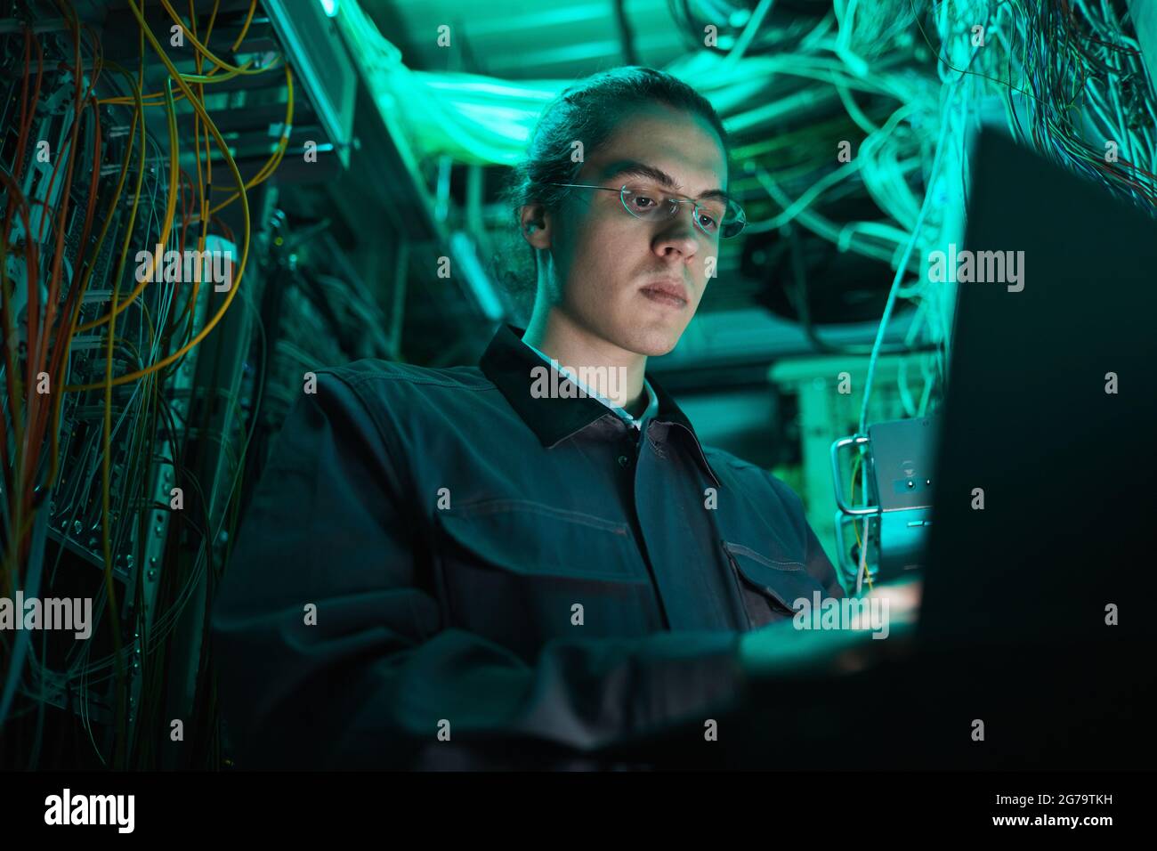 Porträt eines jungen Netzwerktechnikers, der im Serverraum einen Laptop verwendet, während er im Rechenzentrum einen Supercomputer aufsetzt Stockfoto